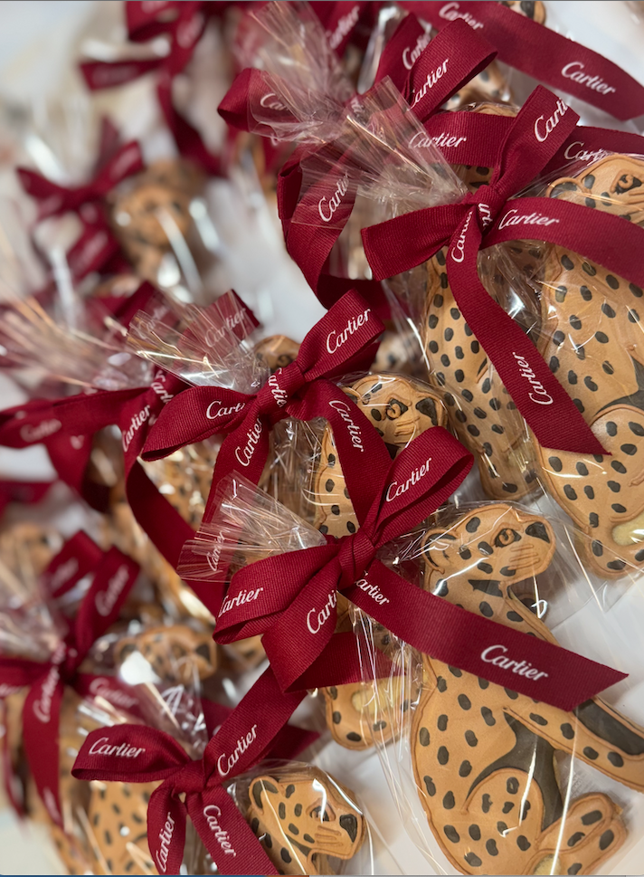 Cookies decorated as cheetahs, wrapped in clear plastic and tied with a red ribbon that says Cartier.