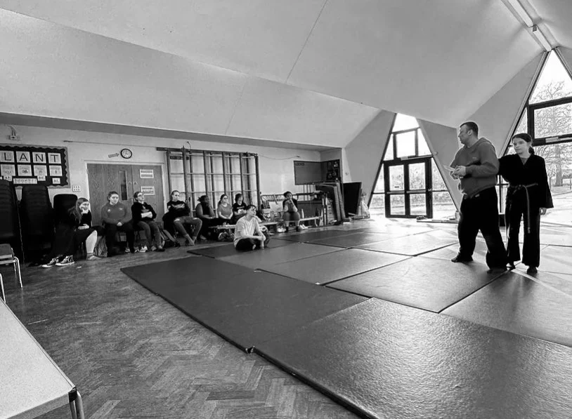 Two individuals practicing self-defense, with bold graphic elements and text in English and Japanese promoting self-defense courses.