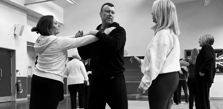 Martial arts training with three people practicing techniques, featuring bold red paint strokes and text "Senior Budo Taijutsu" in English and Japanese.