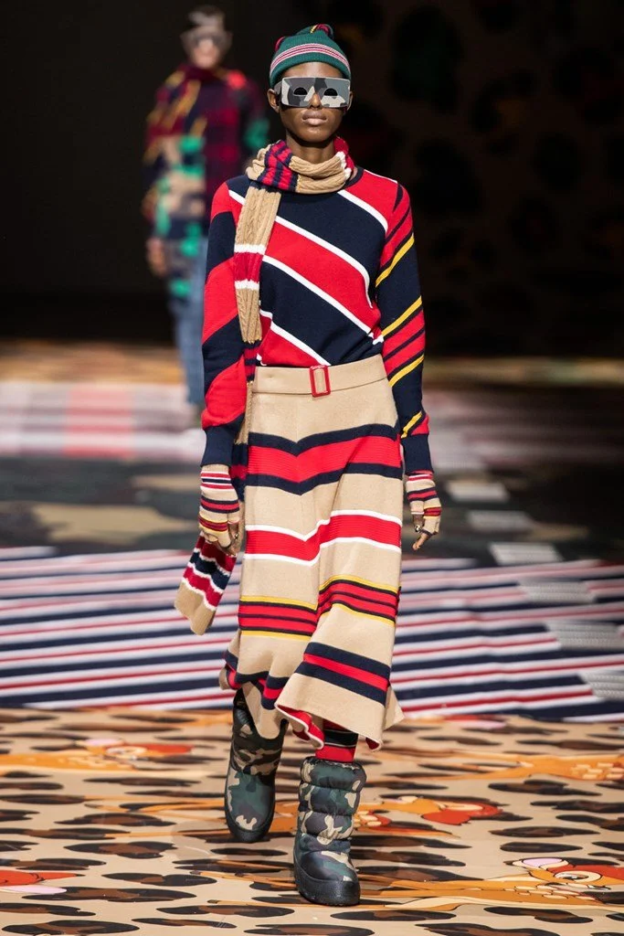 Modella sulla passerella di moda con abbigliamento colorato e accessori distintivi.