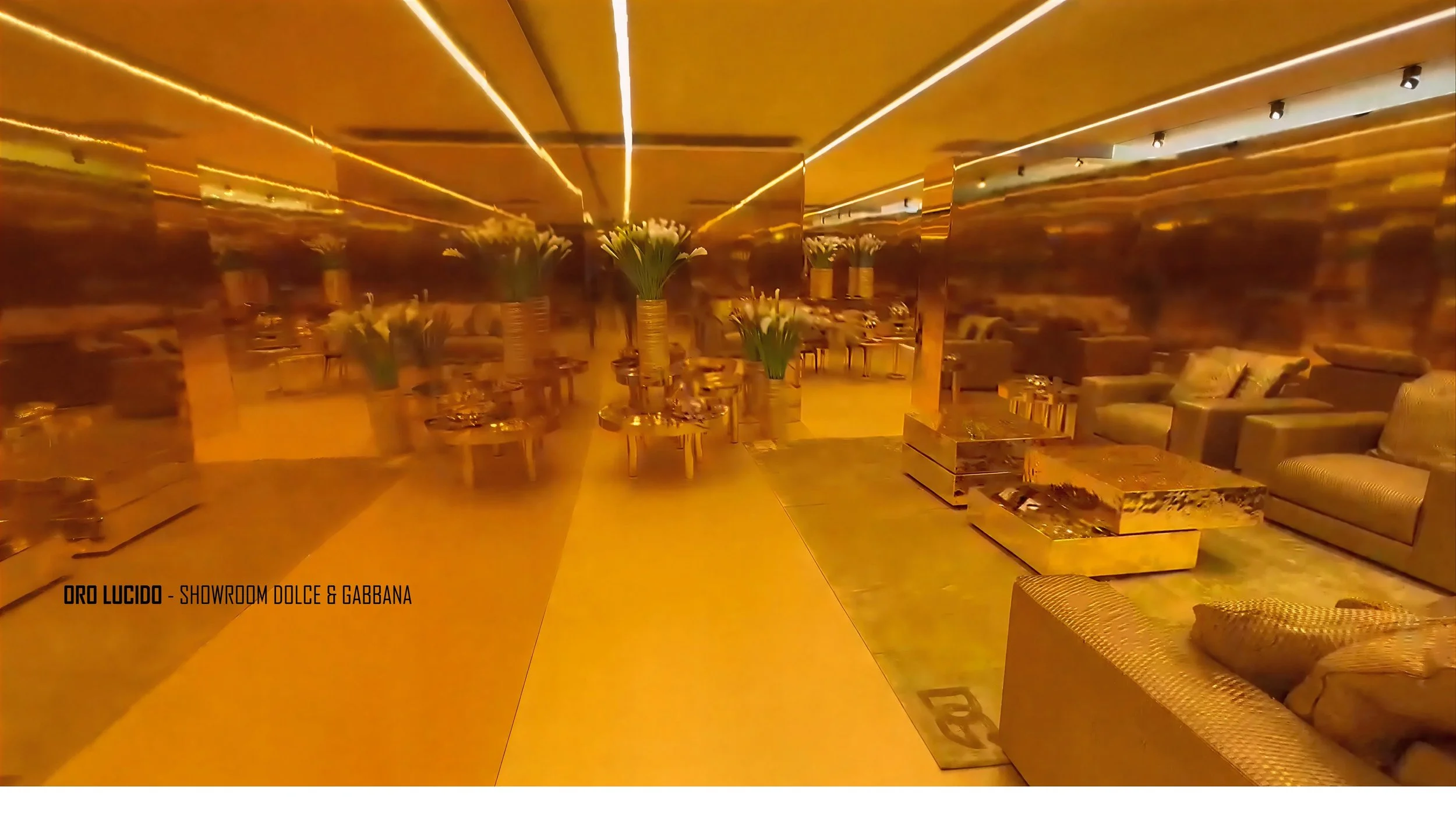 Interno di un salone con arredamento di lusso in oro lucido, divani, tavolini di marmo e vasi con fiori, illuminazione calda.