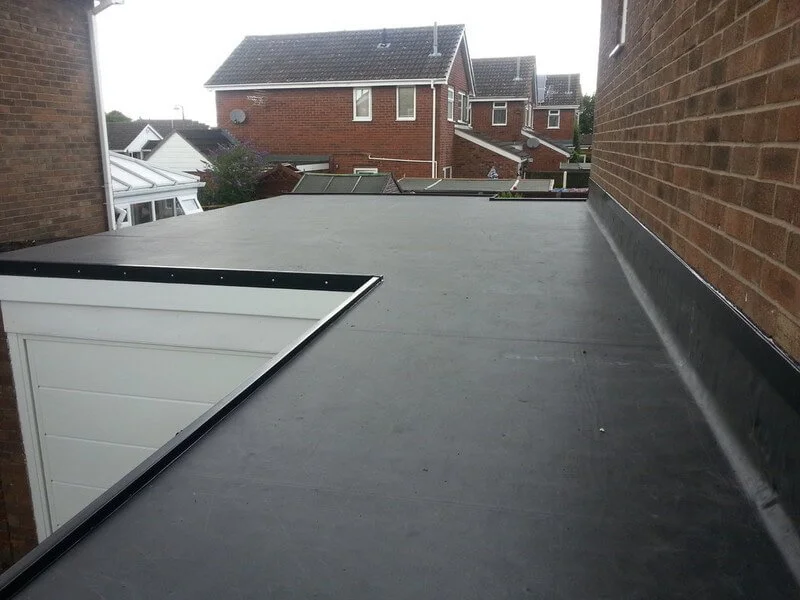 View of a flat roof on a house with surrounding brick walls and neighbouring houses in the background