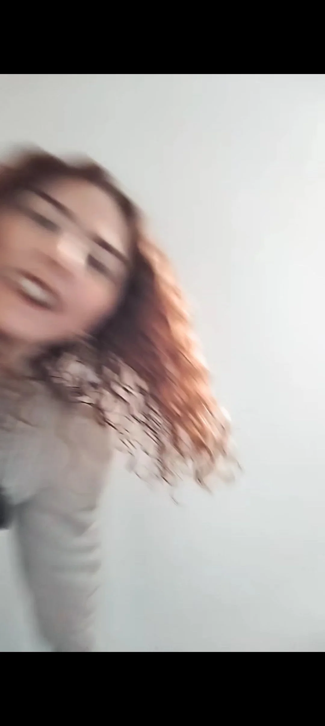 Blurry photo of a woman with curly hair smiling and in motion, against a plain white background.