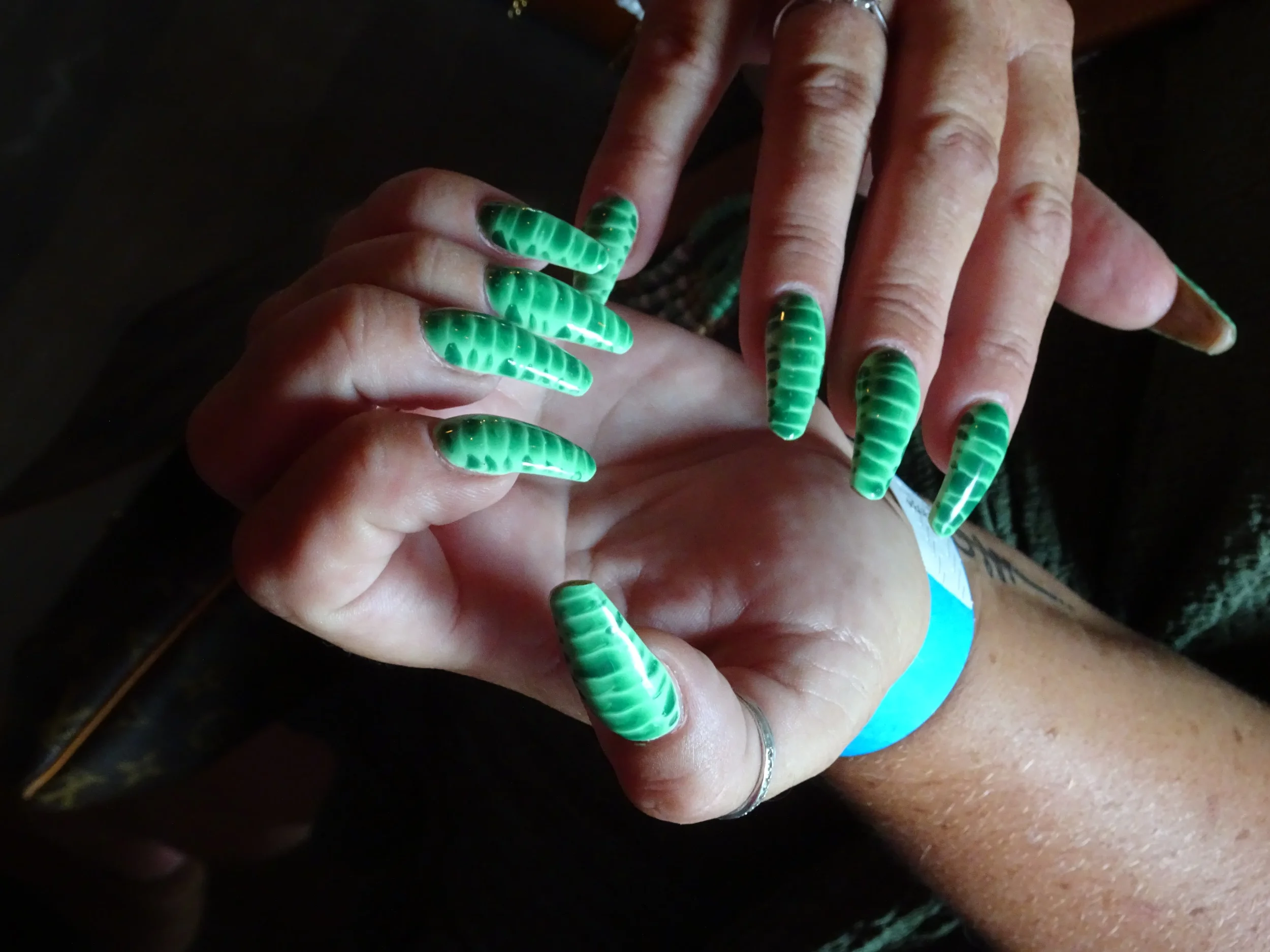 Close-up of a person's hands with long, green, zebra-like patterned acrylic nails.