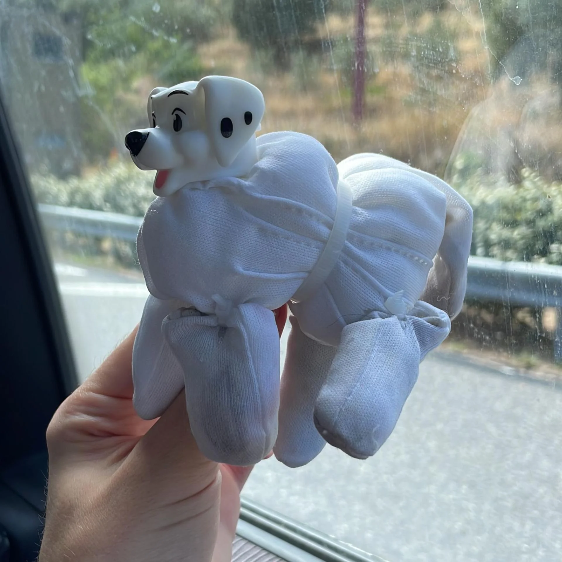 A small stuffed dog toy with a cartoonish face, held inside a hand. The toy is attached to a white sock or cloth with arms and legs, possibly representing a dog.