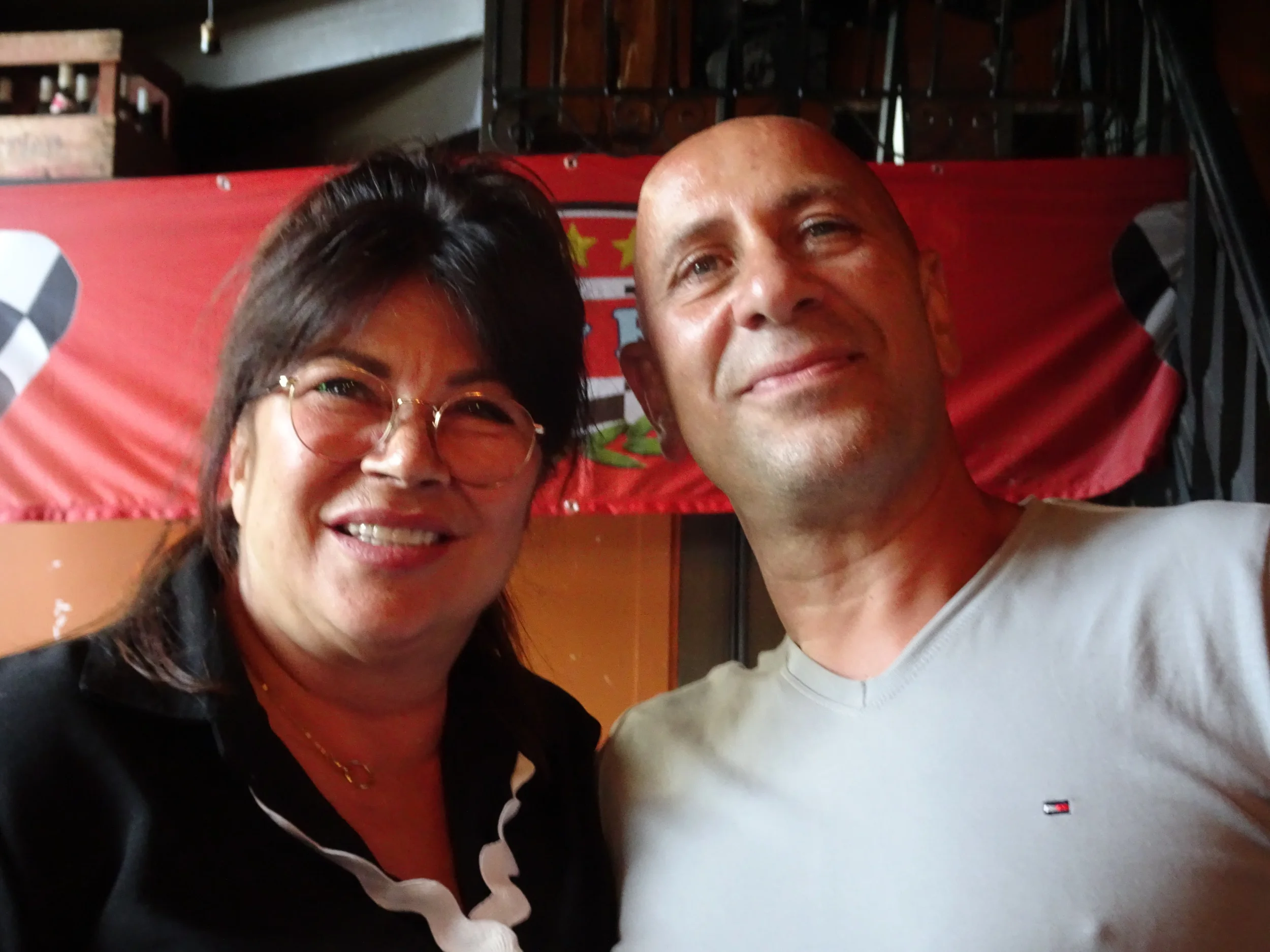 A woman with glasses and a man in a white shirt smiling for a selfie indoors.