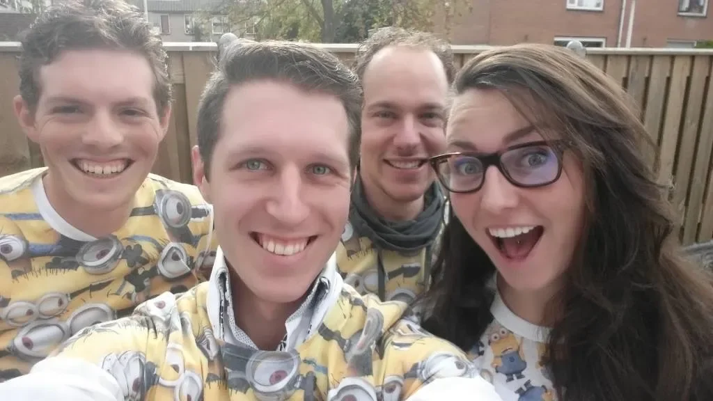 Four friends smiling and taking a group selfie outdoors, wearing matching Minions-themed shirts.