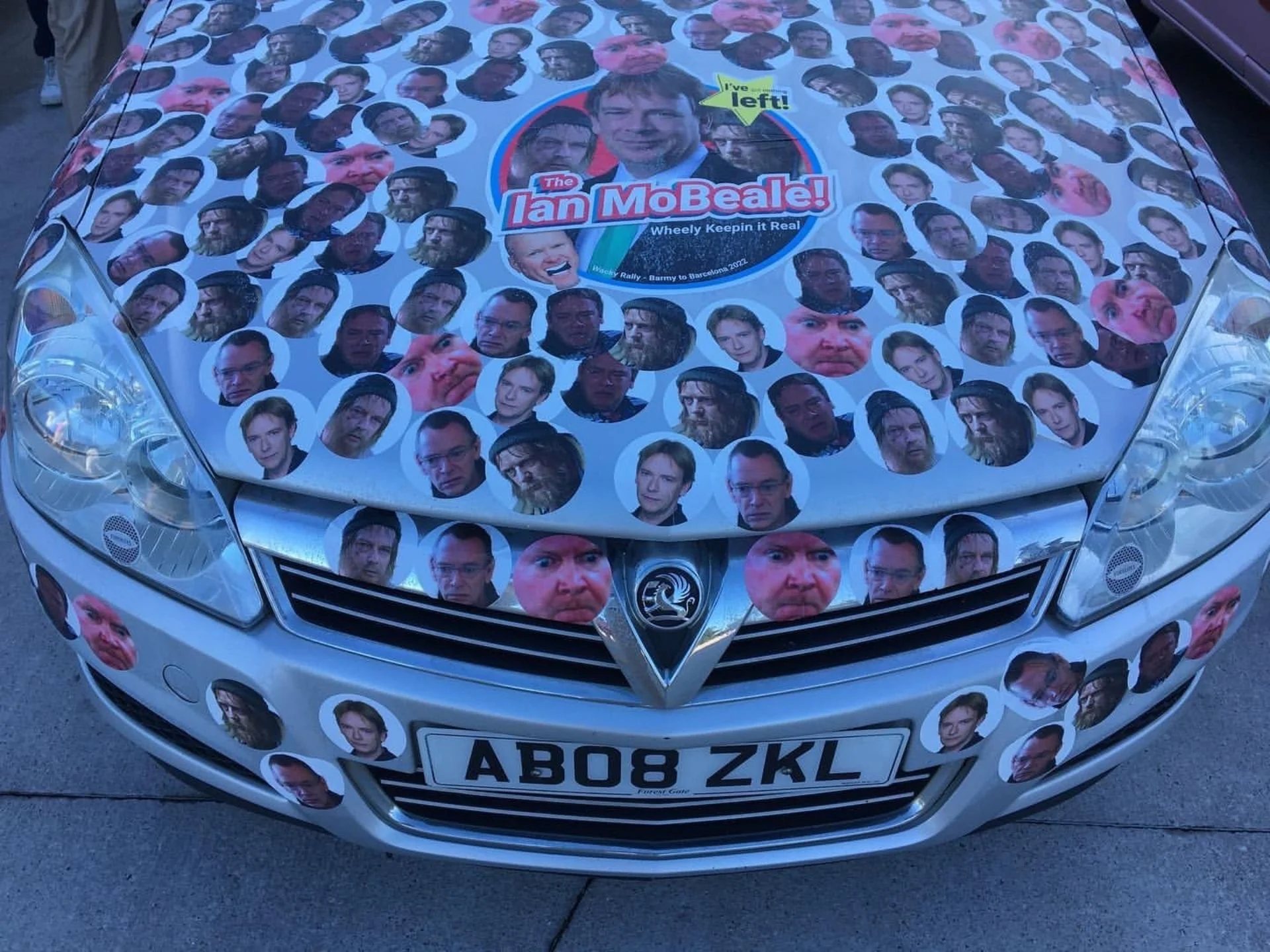 A car with a large decal on the hood featuring numerous small photos of sees of Ian Mo Beale from the TV show EastEnders, along with a central circle with the text 'I've left! The Ian MoBeale! Wheely Keepin it Real' and references to a rally from Bar
