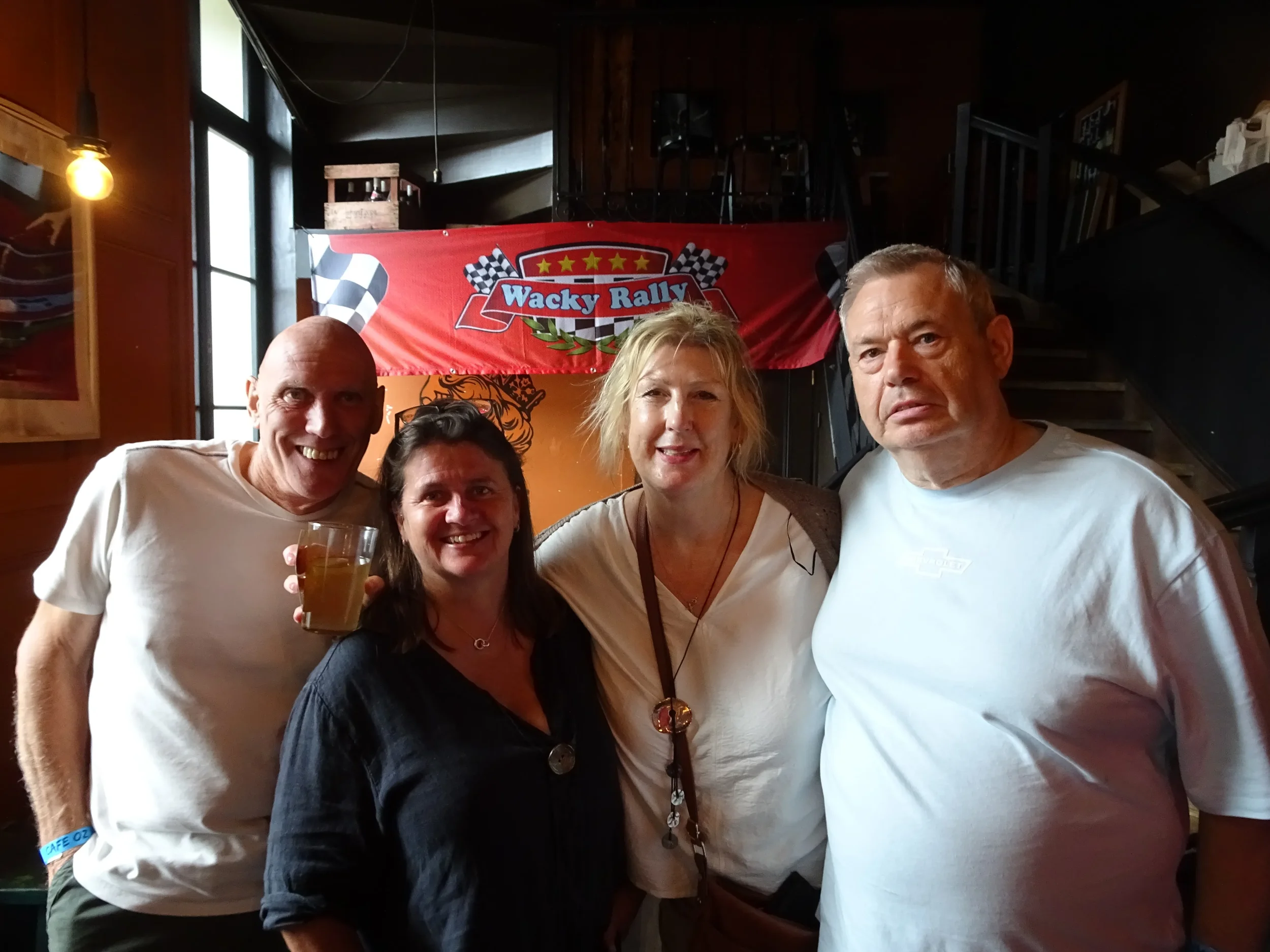 Four people smiling and posing for a photo indoors, with a banner reading 'Wacky Rally' in the background.