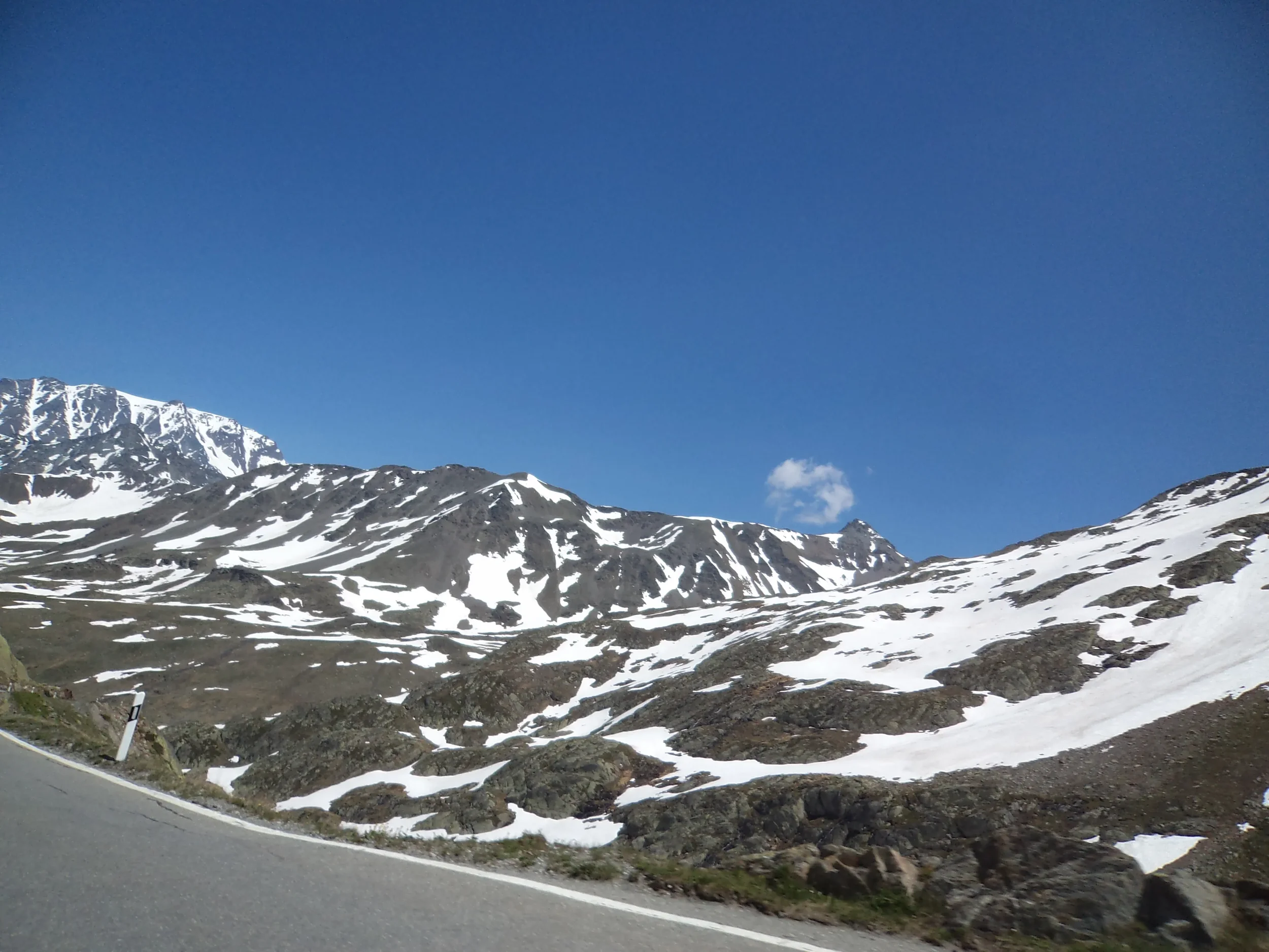 Snowy mountain landscape with a clear blue sky and a winding road in the foreground.