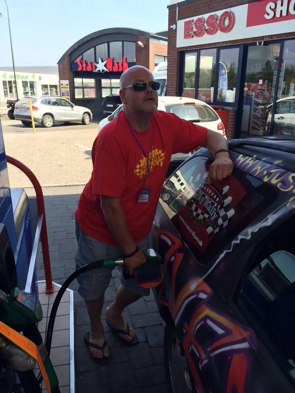 Man filling gas tank at a gas station in front of a convenience store with signs for Esso and Star Wash.