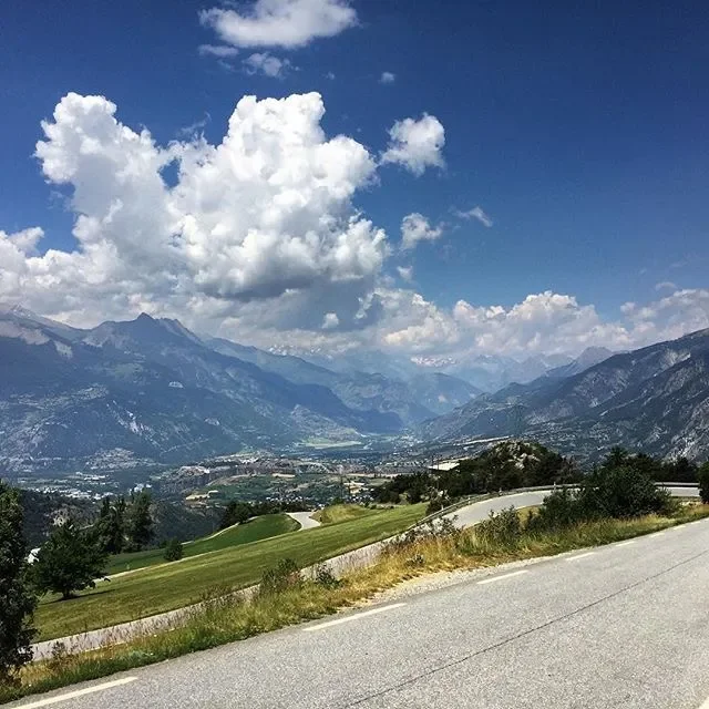 A scenic view of mountains, a valley, a winding road, and a partly cloudy sky.