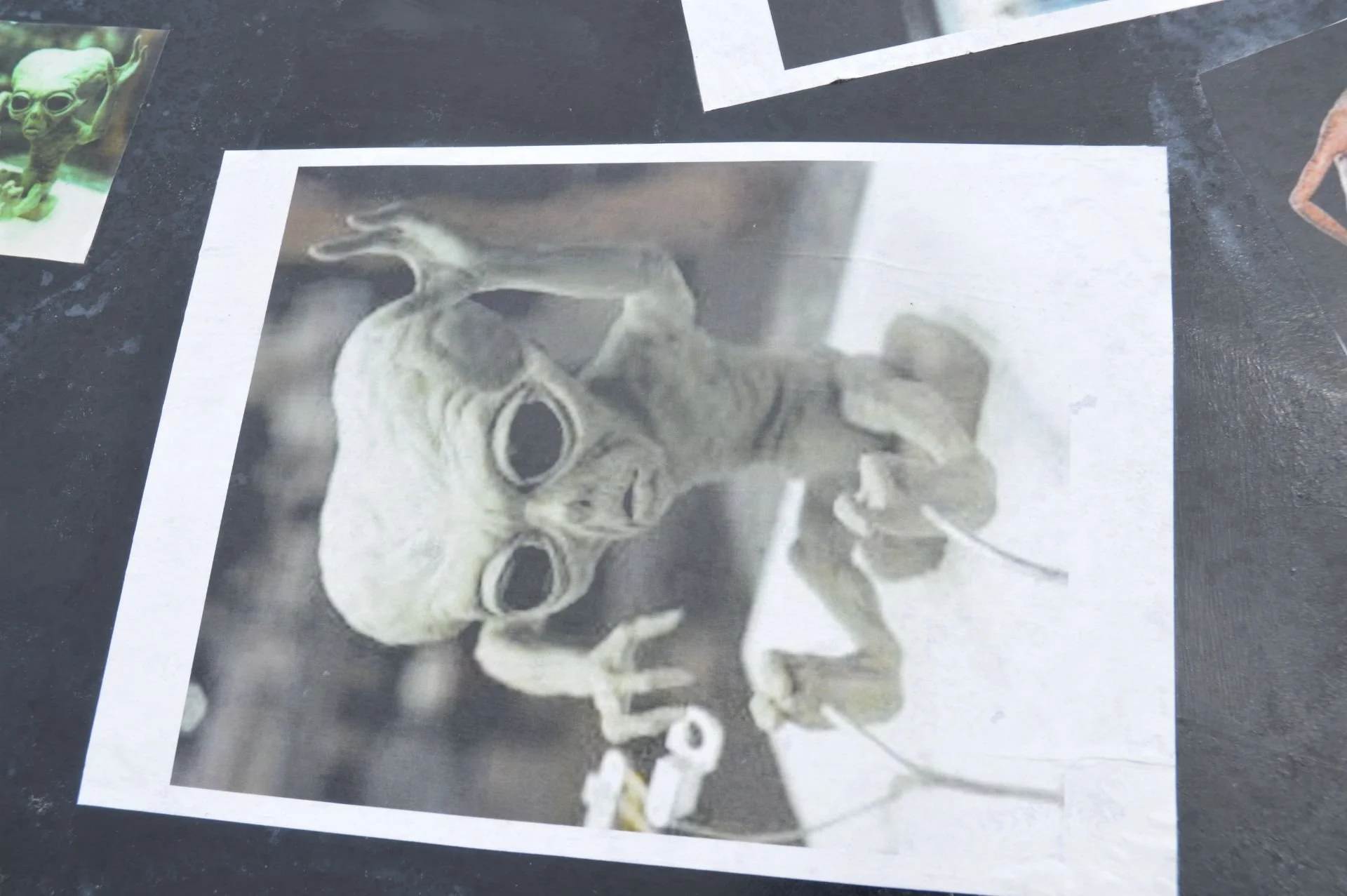 A black and white photo of a baby alien creature with large eyes and elongated head, sitting and holding a small object.