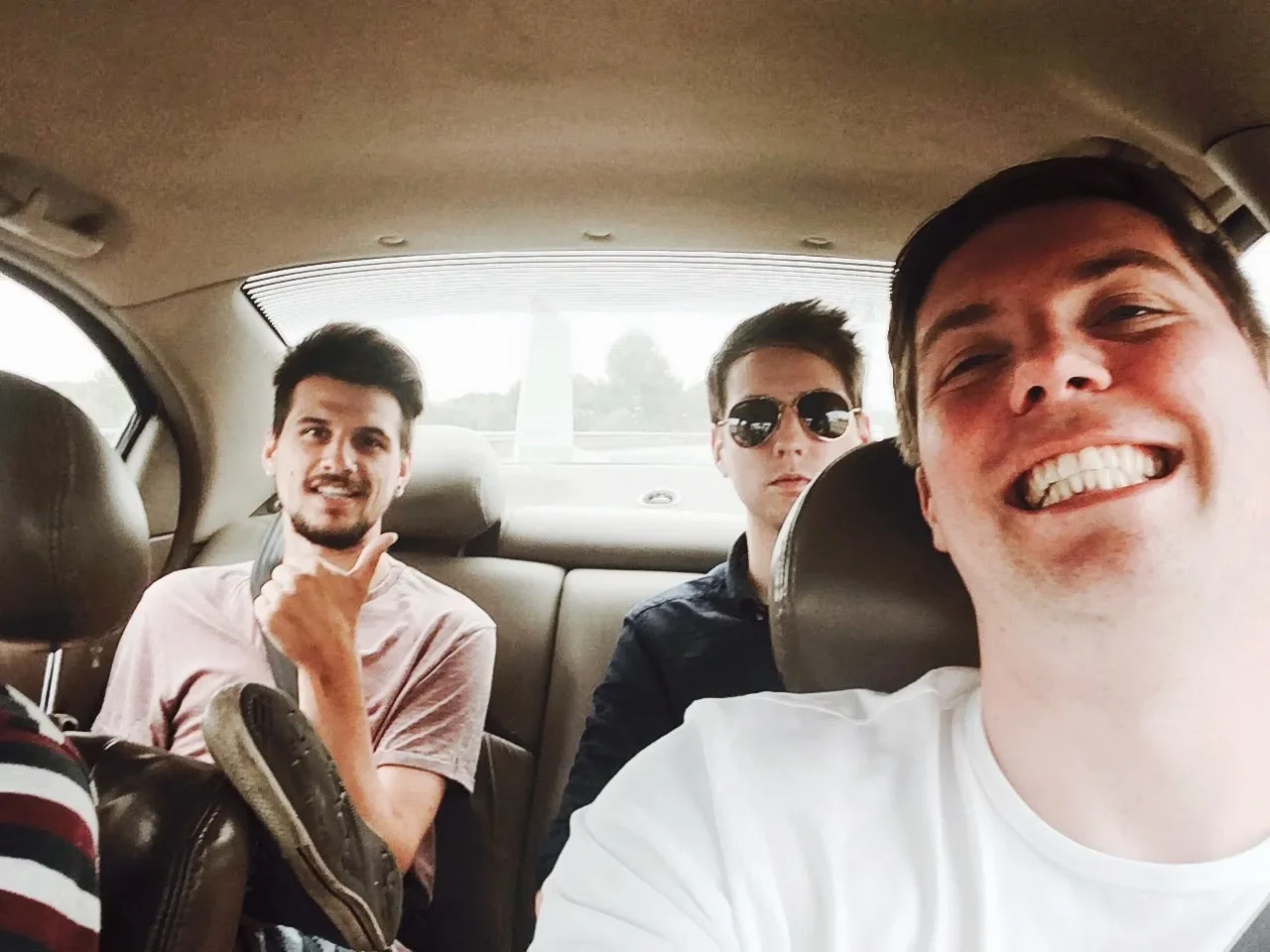 Three young men sitting in the backseat of a car, smiling and appearing happy.