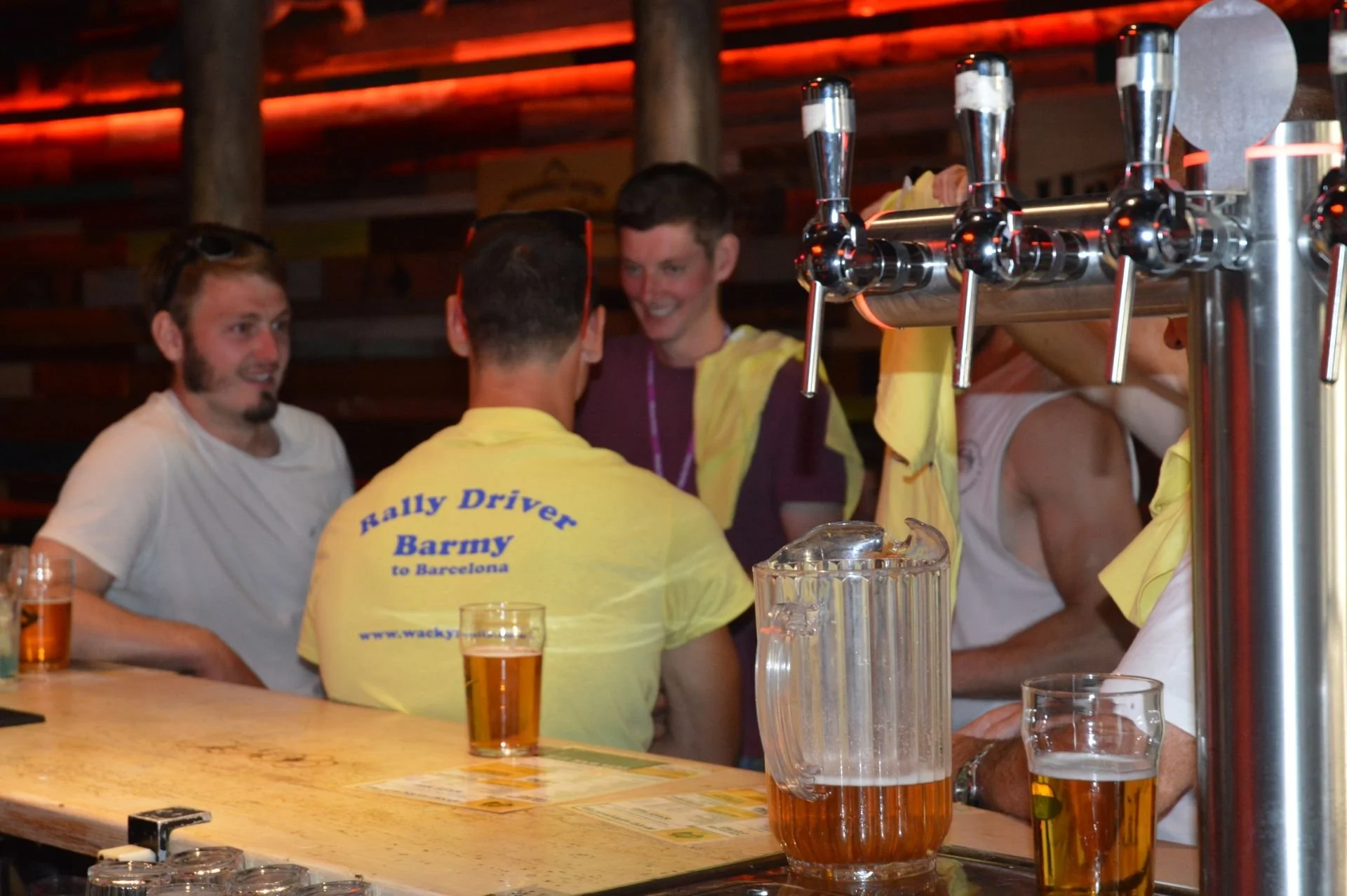 Group of men socializing at a bar with beer on the counter, wooden paneling, and beer taps in a cozy pub setting.