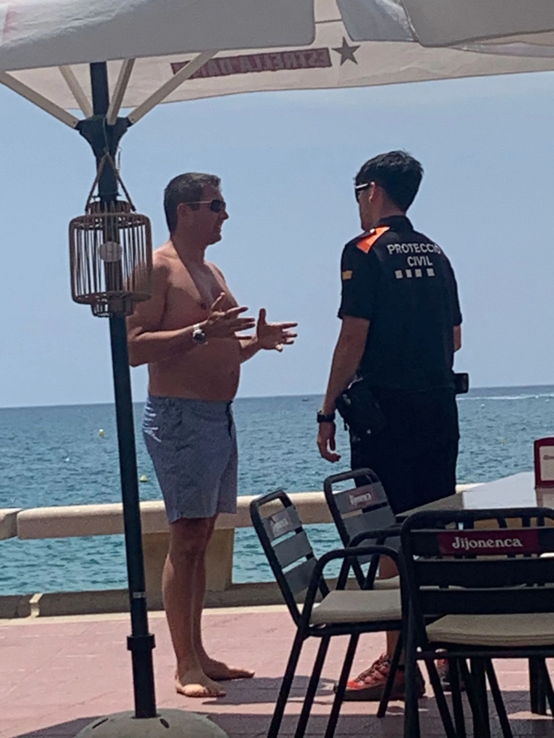 A man in swim shorts talking to a lifeguard at the beach during daytime.