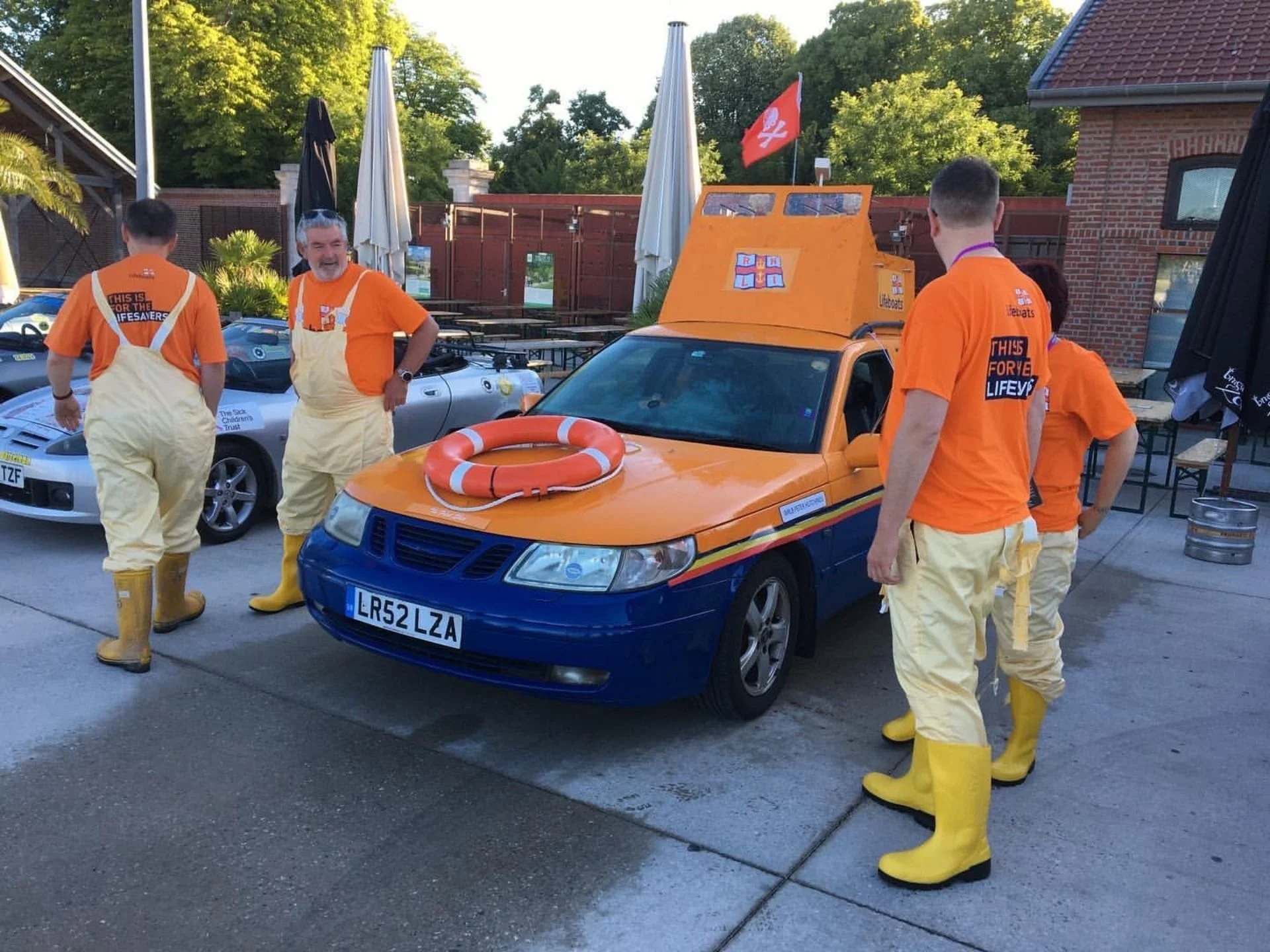 Group of people dressed as lifeguards standing around a car converted into a lifeboat with a lifebuoy on the hood.