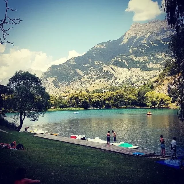 People relaxing by a dock on a lake surrounded by trees with mountains in the background.