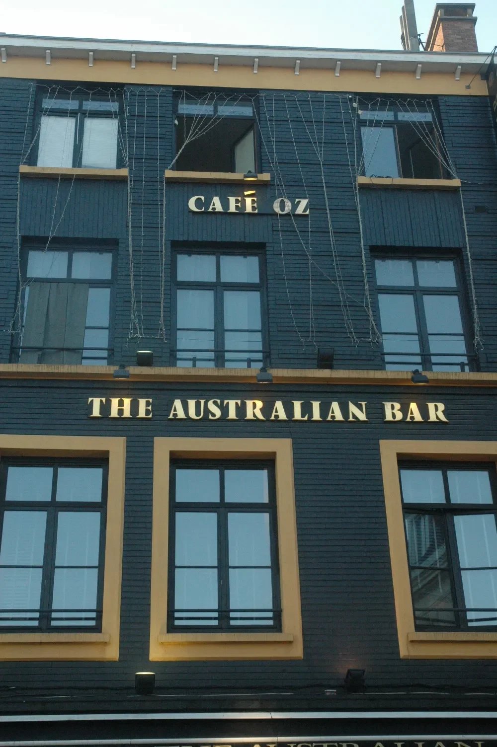 The exterior of a building with the sign "Café ÖZ" and "The Australian Bar" on it, with blue walls and multiple windows.