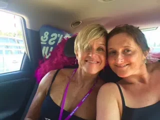 Two women sitting closely together inside a vehicle, smiling at the camera.