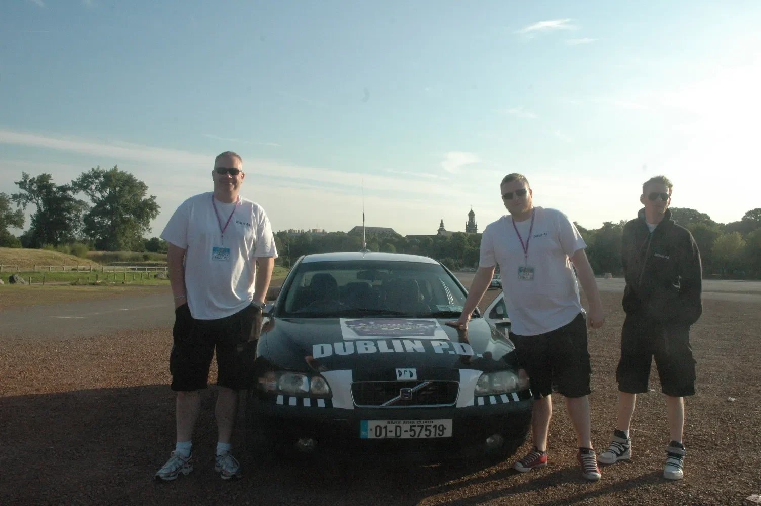 Three men standing next to a black car with 