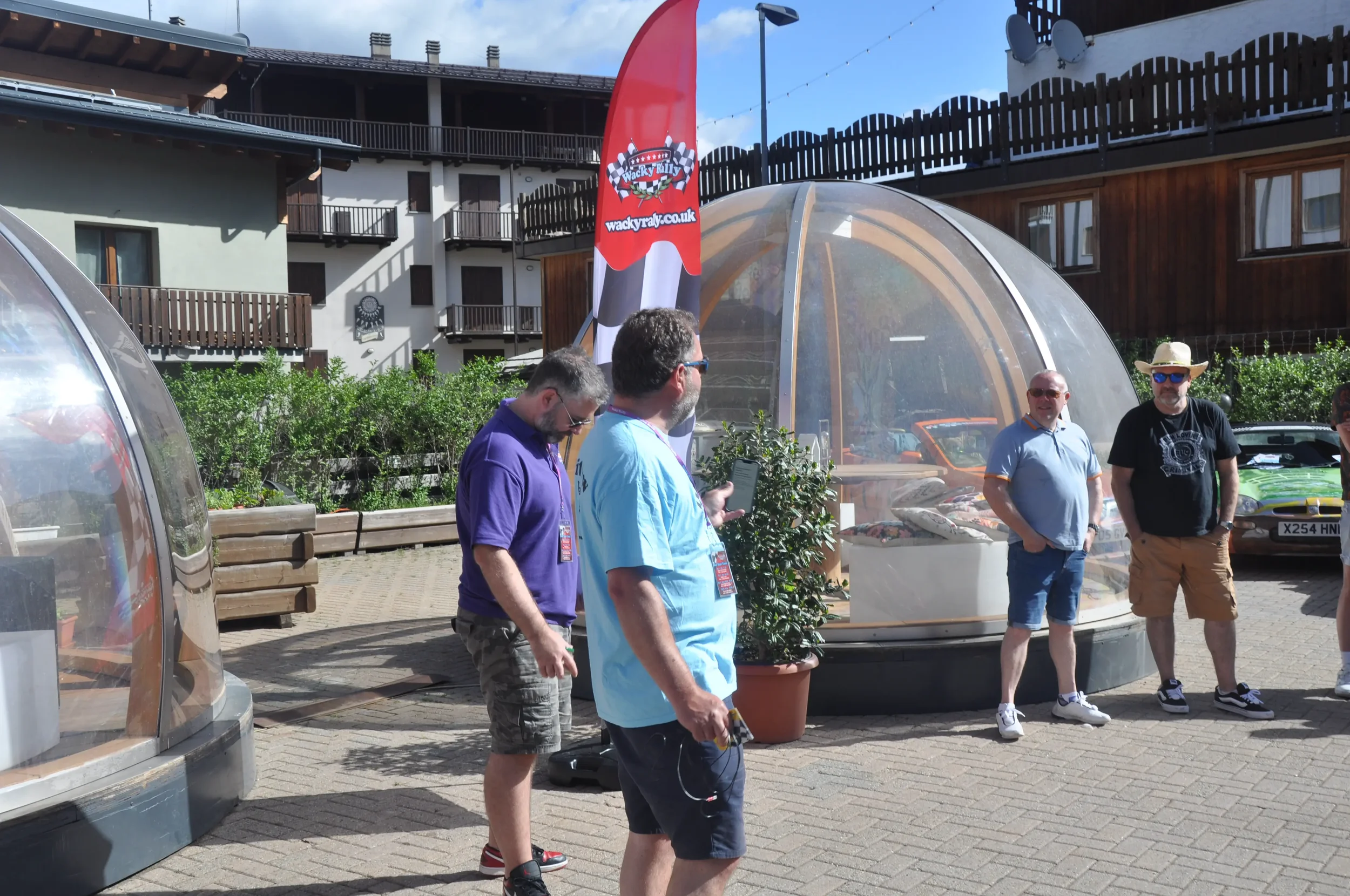 People standing outdoors near a transparent dome-shaped structure with a flag that reads "Wacky Races".