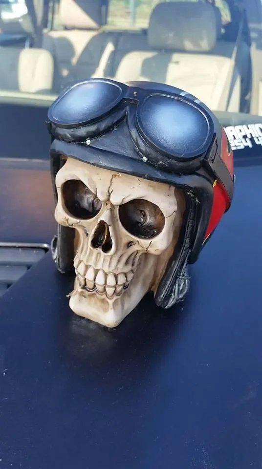 A skull with a motorcycle helmet and goggles resting on a vehicle dashboard.