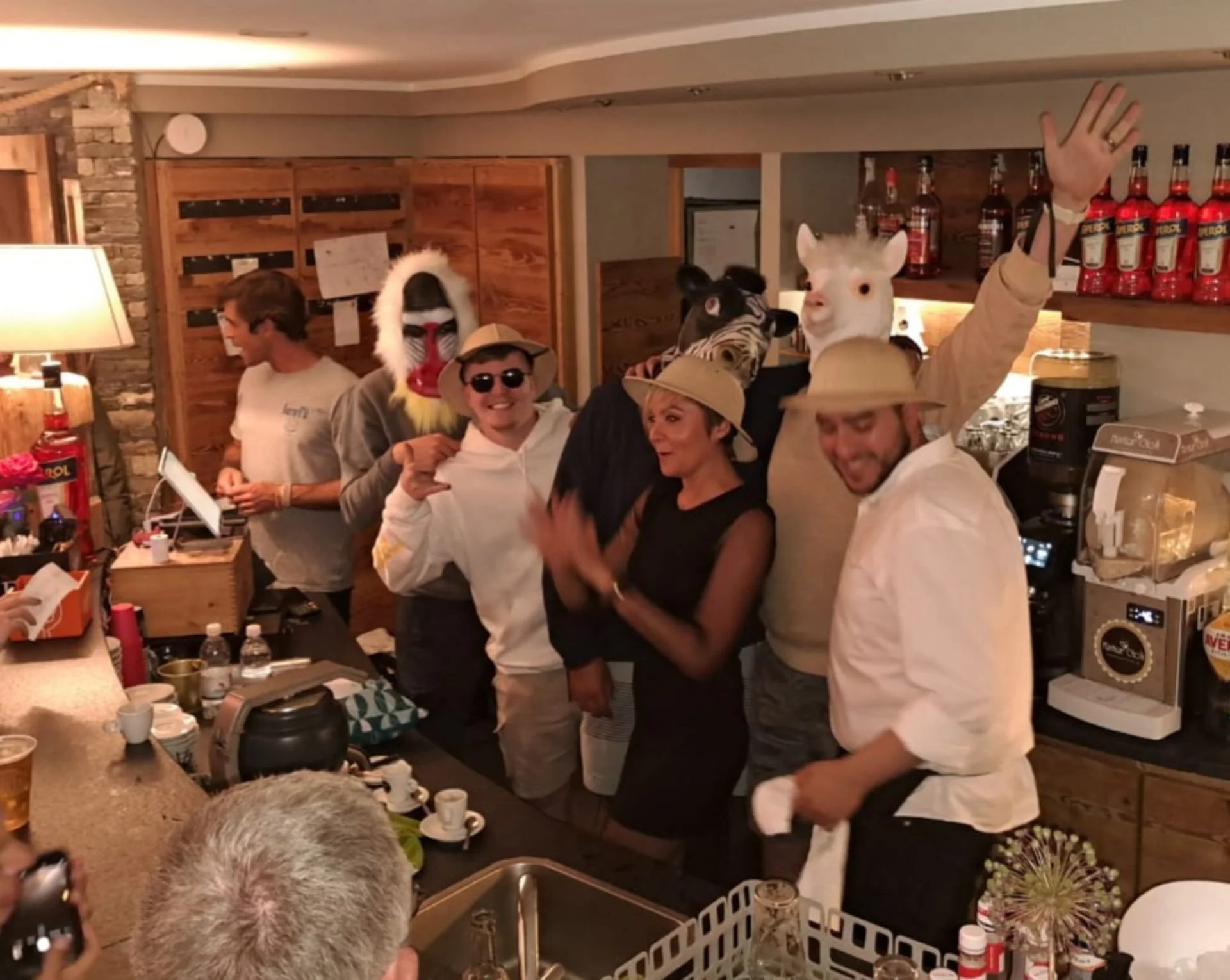 Group of people in costumes with animal masks, taking selfies and celebrating in a bar or restaurant.