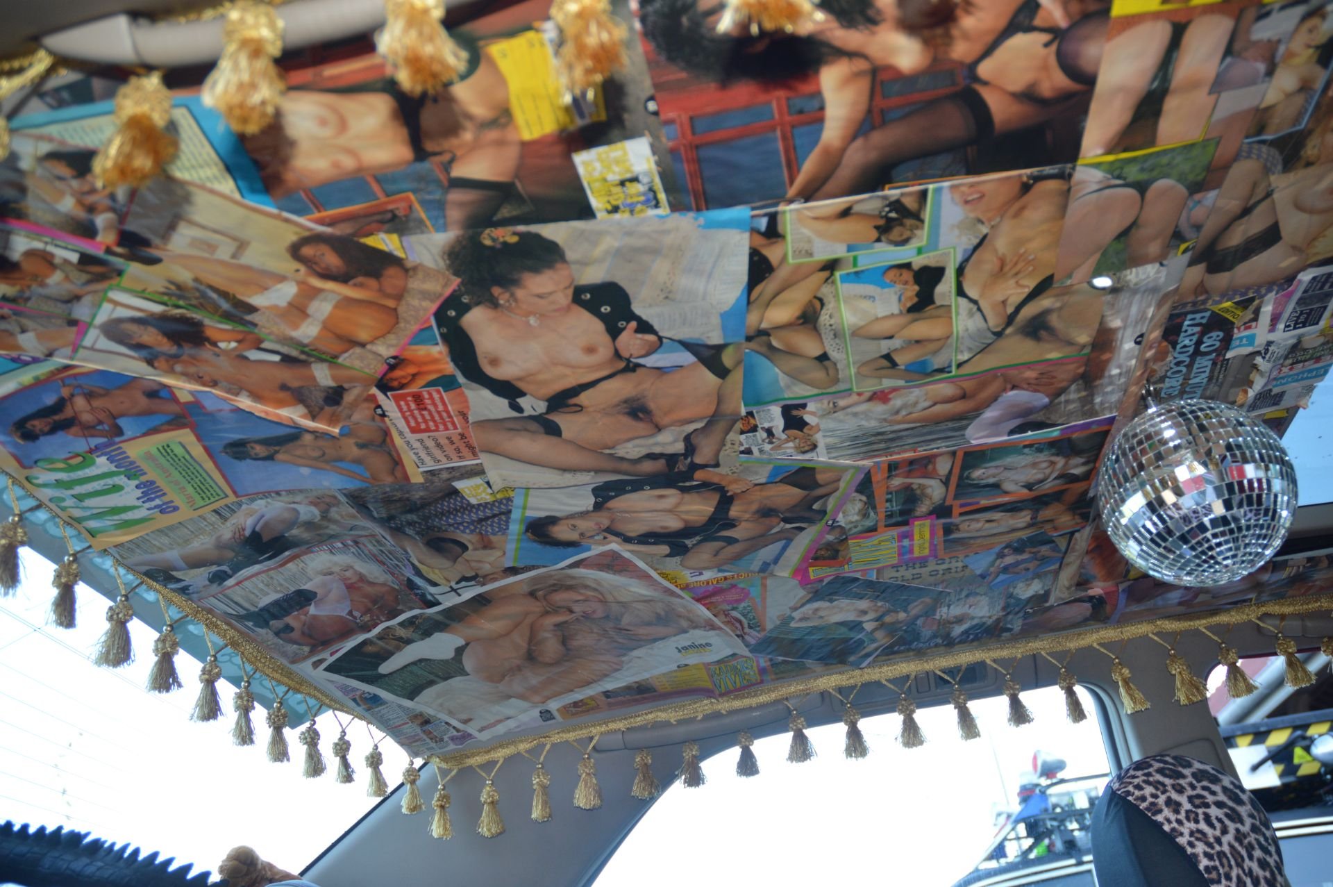 Ceiling decorated with adult magazine pages, surrounded by tassels, with a disco ball hanging in the vehicle interior.
