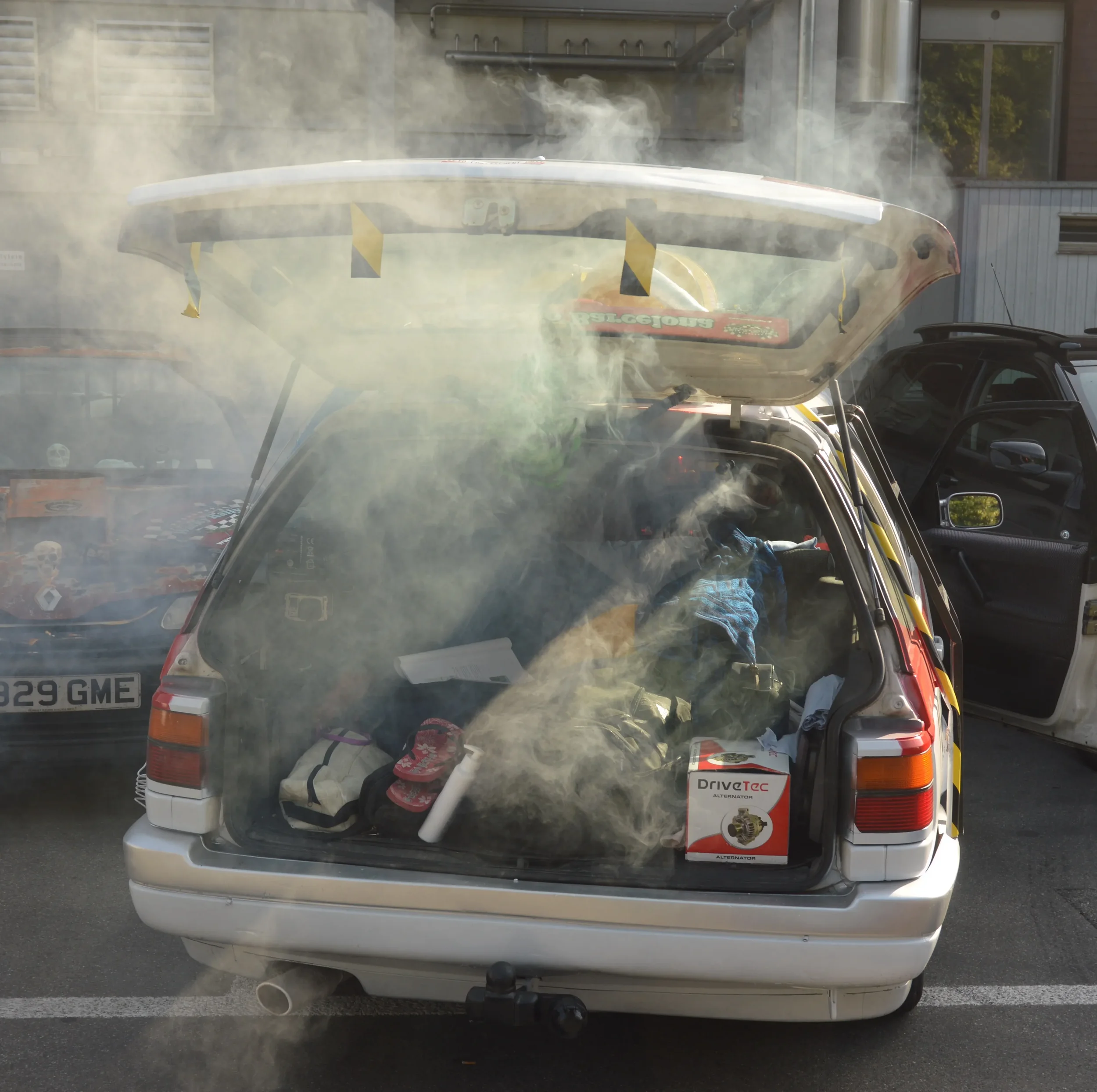 The rear of a car with the trunk open, filled with various items and surrounded by smoke or fog.