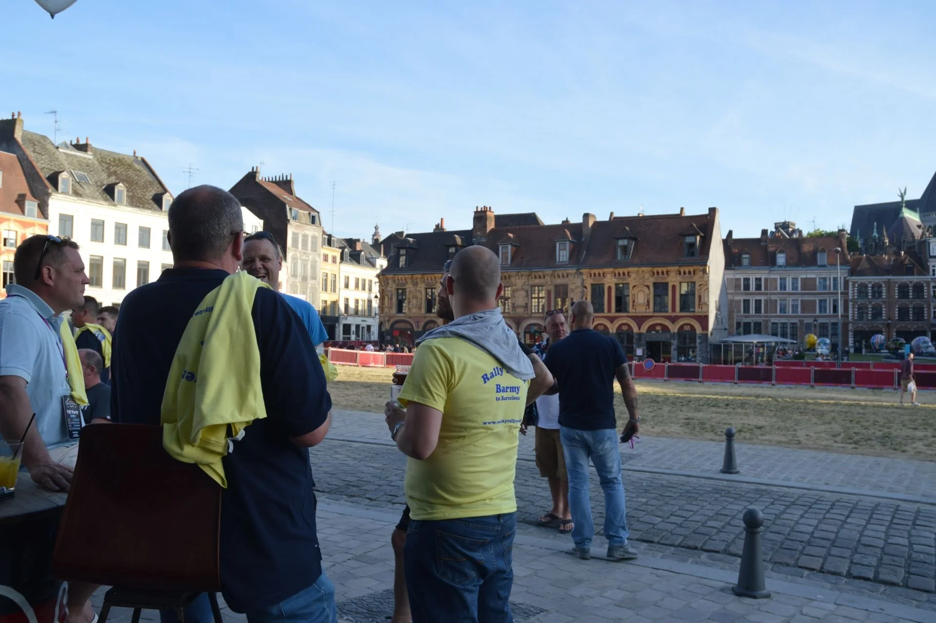 Group of people gathered in an outdoor urban setting, talking and laughing, with historic buildings and blue sky in the background.