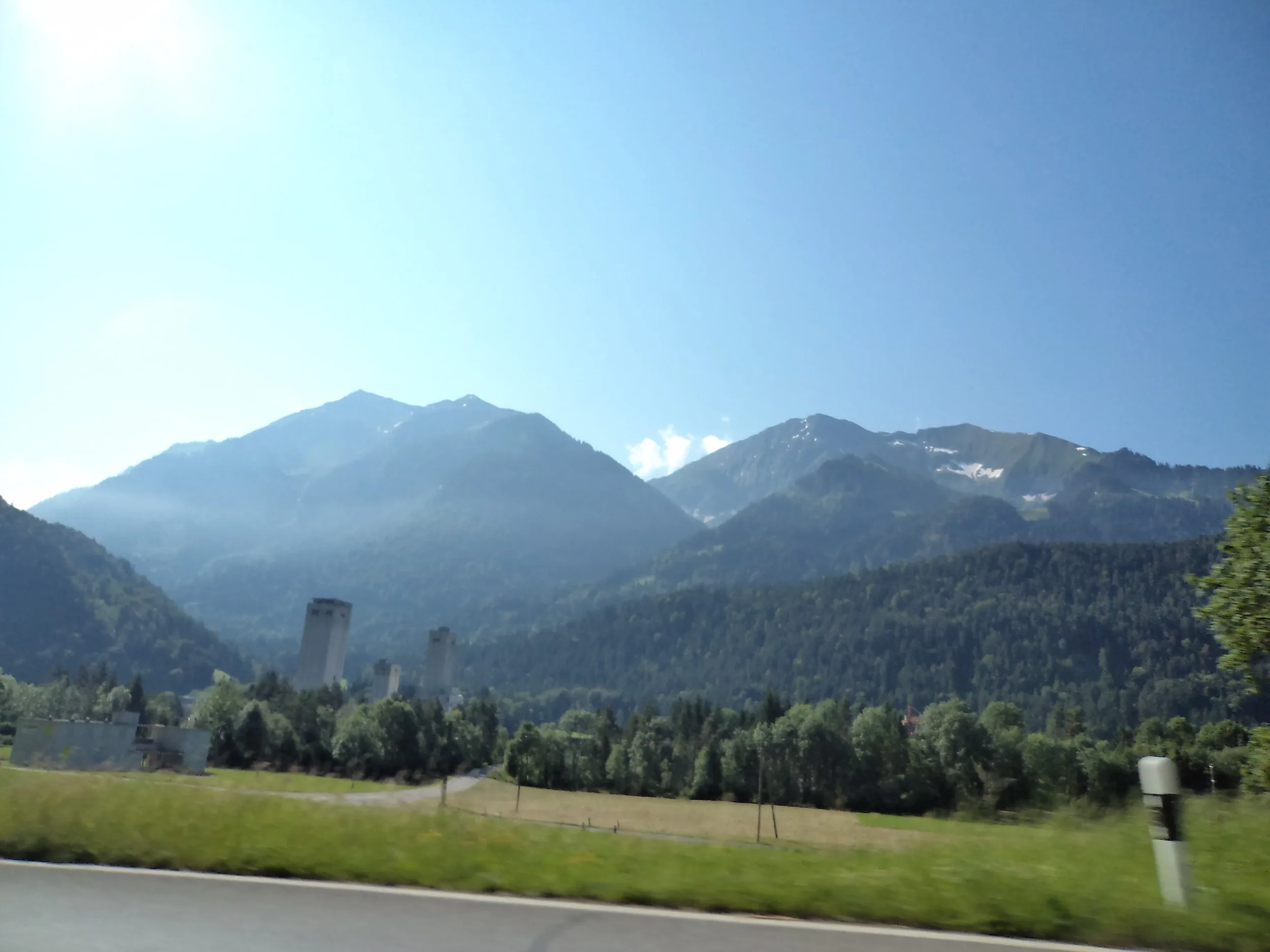Scenic view of a mountain range with lush greenery in the foreground, a clear blue sky, and some snow patches on the peaks.