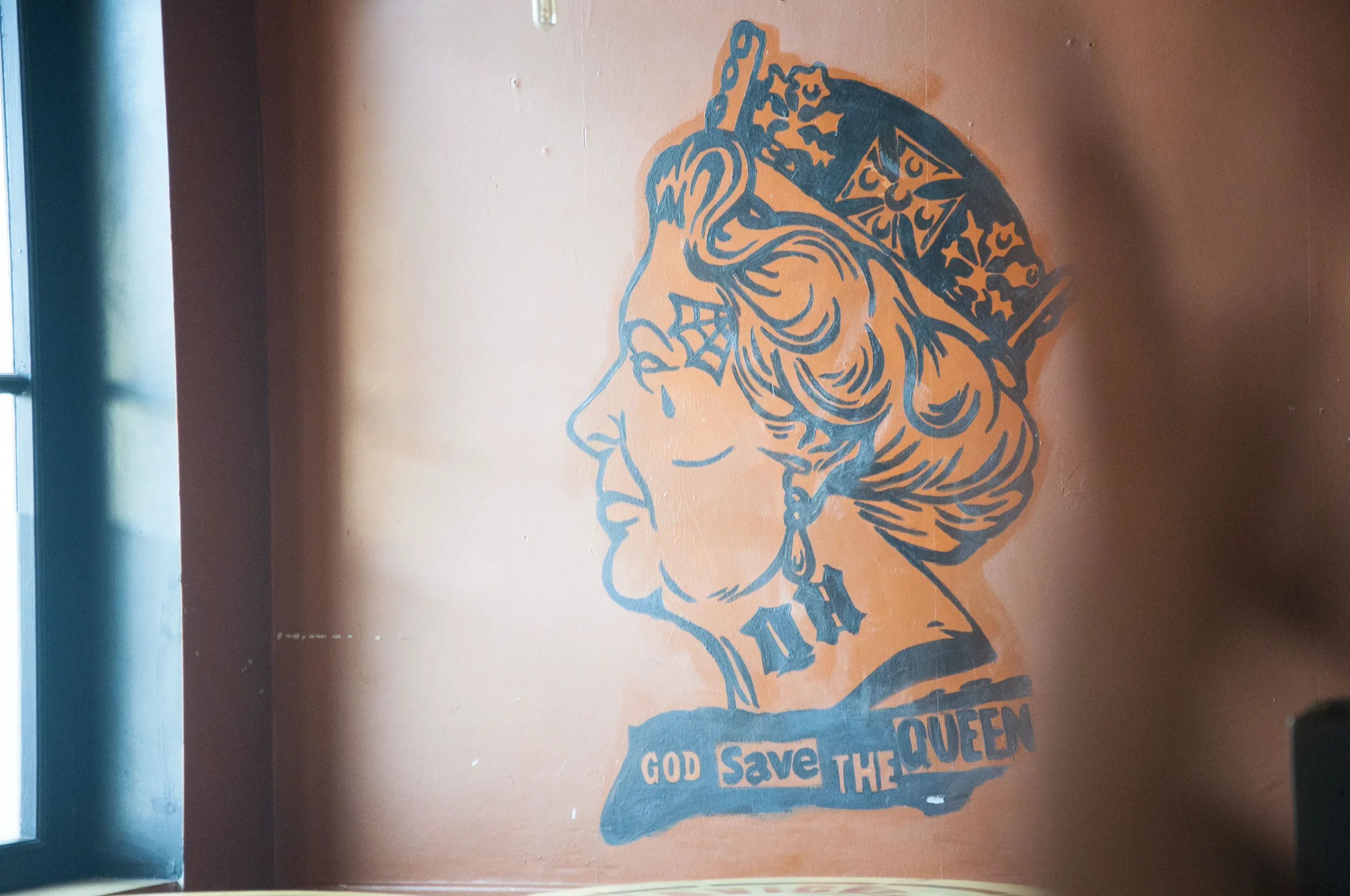 Wall art depicting a woman's profile with a crown or tiara, tear falling from eye, and the text "God Save the Queen" underneath.