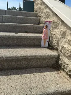 A cardboard cutout of a woman in a pink floral dress leaning against a wall by outdoor concrete stairs.