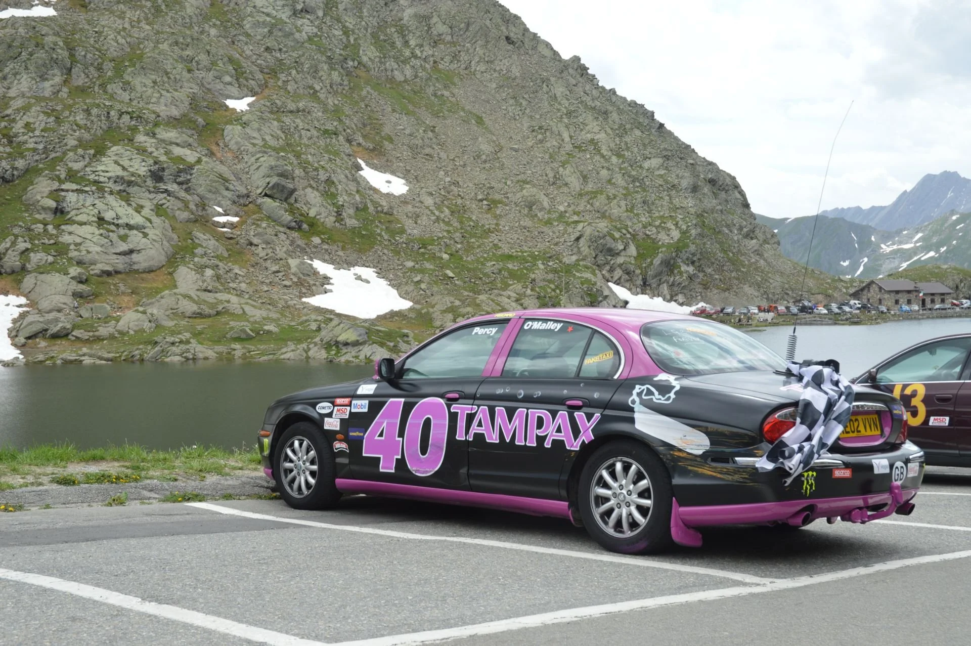 Race car with Tampax logo and number 40 parked by a lake with mountains in the background, overcast sky.