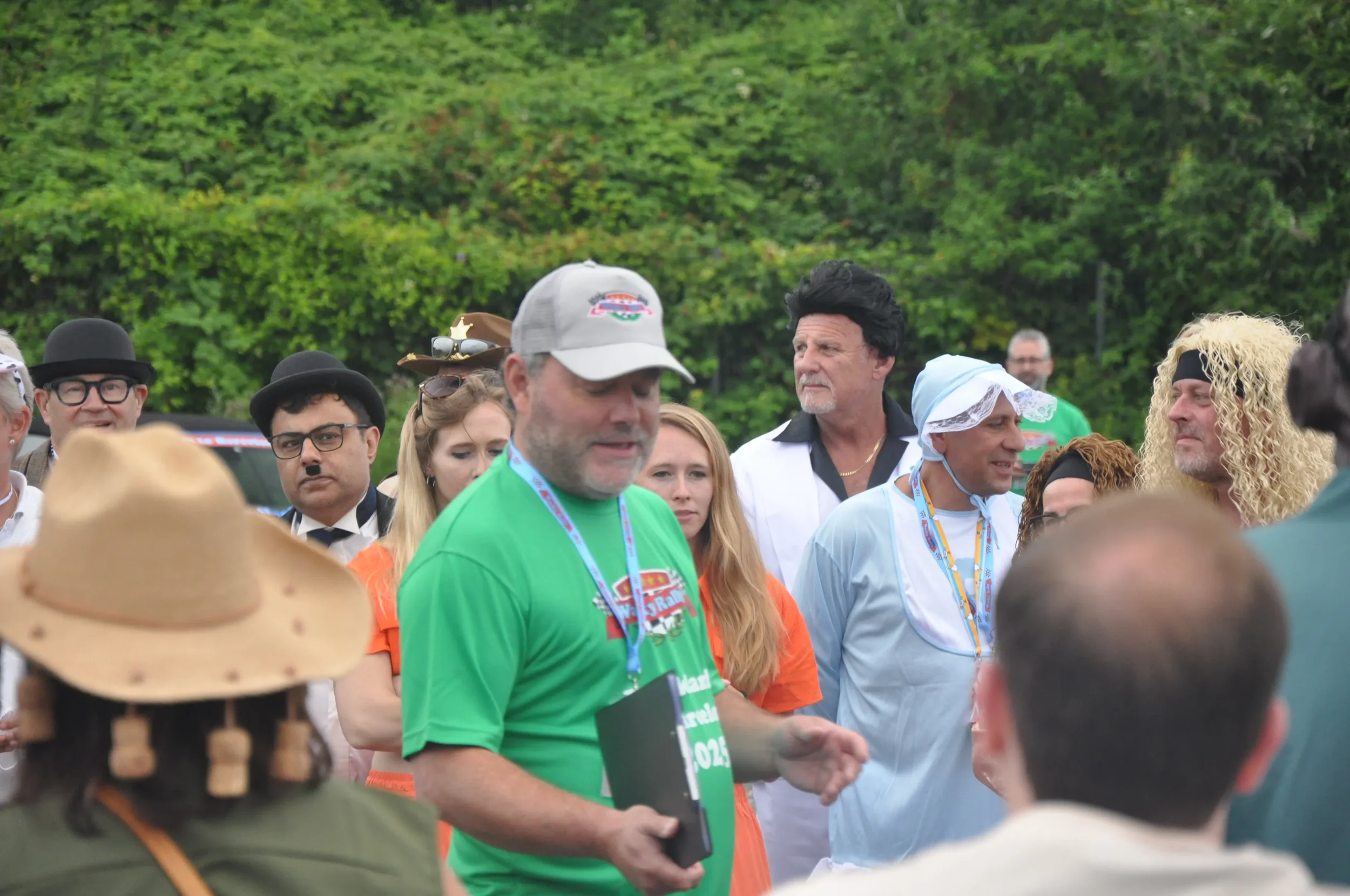 Group of people outdoors dressed in various costumes and casual clothing, with a background of green trees.