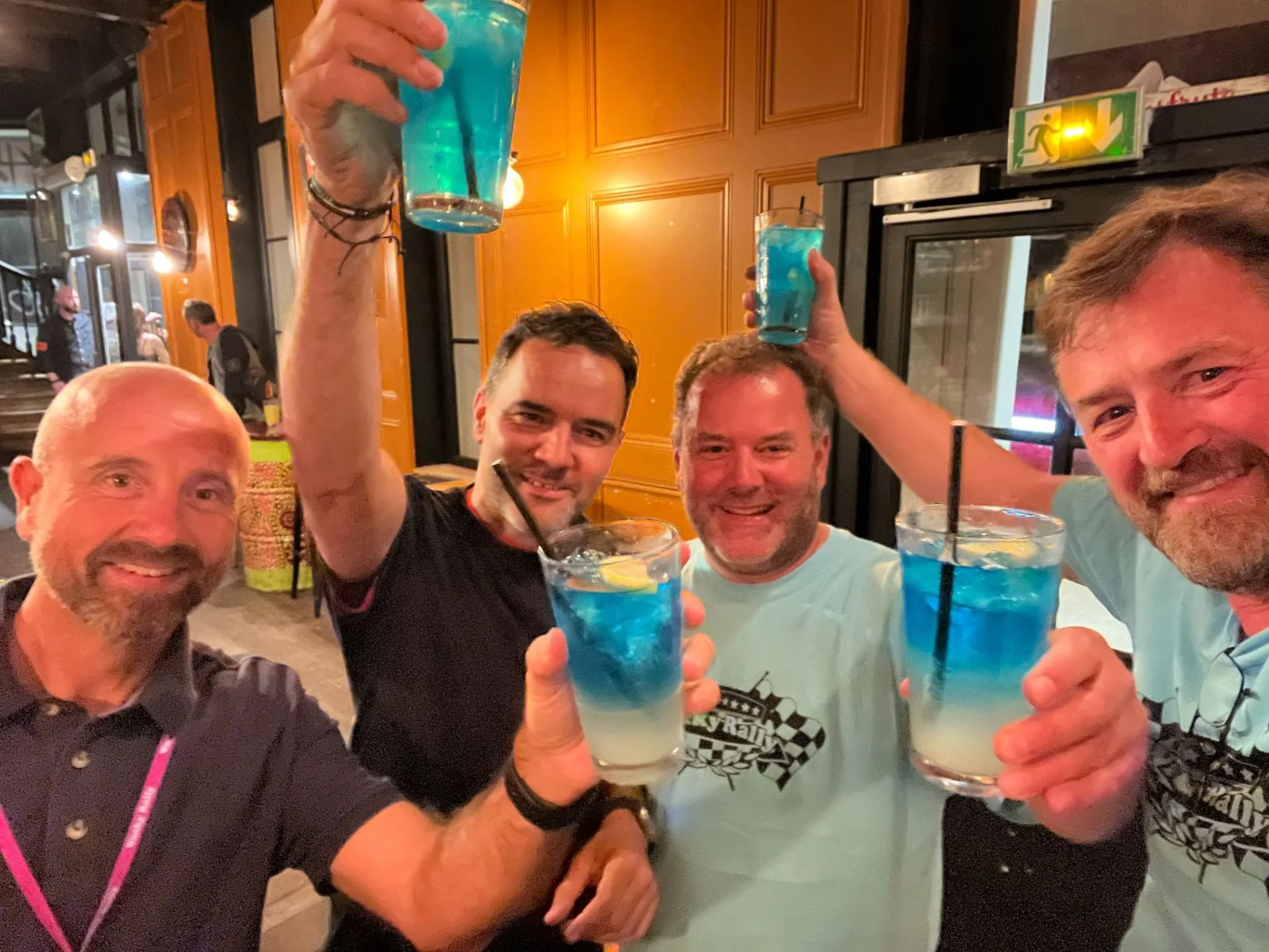 Four men smiling and holding blue and white layered drinks with straws in a bar or restaurant.