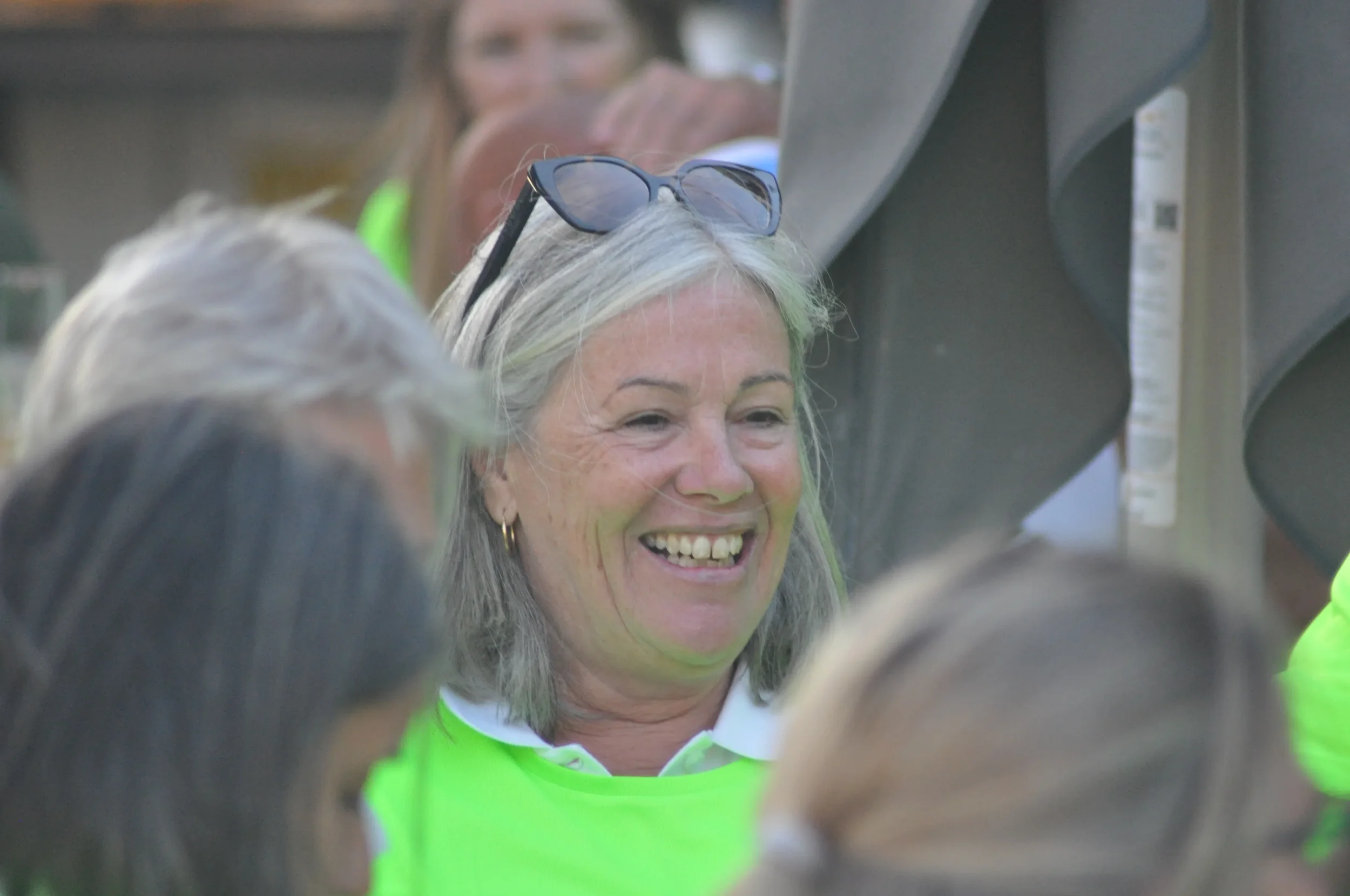 A smiling woman with gray hair wearing sunglasses on her head surrounded by people.