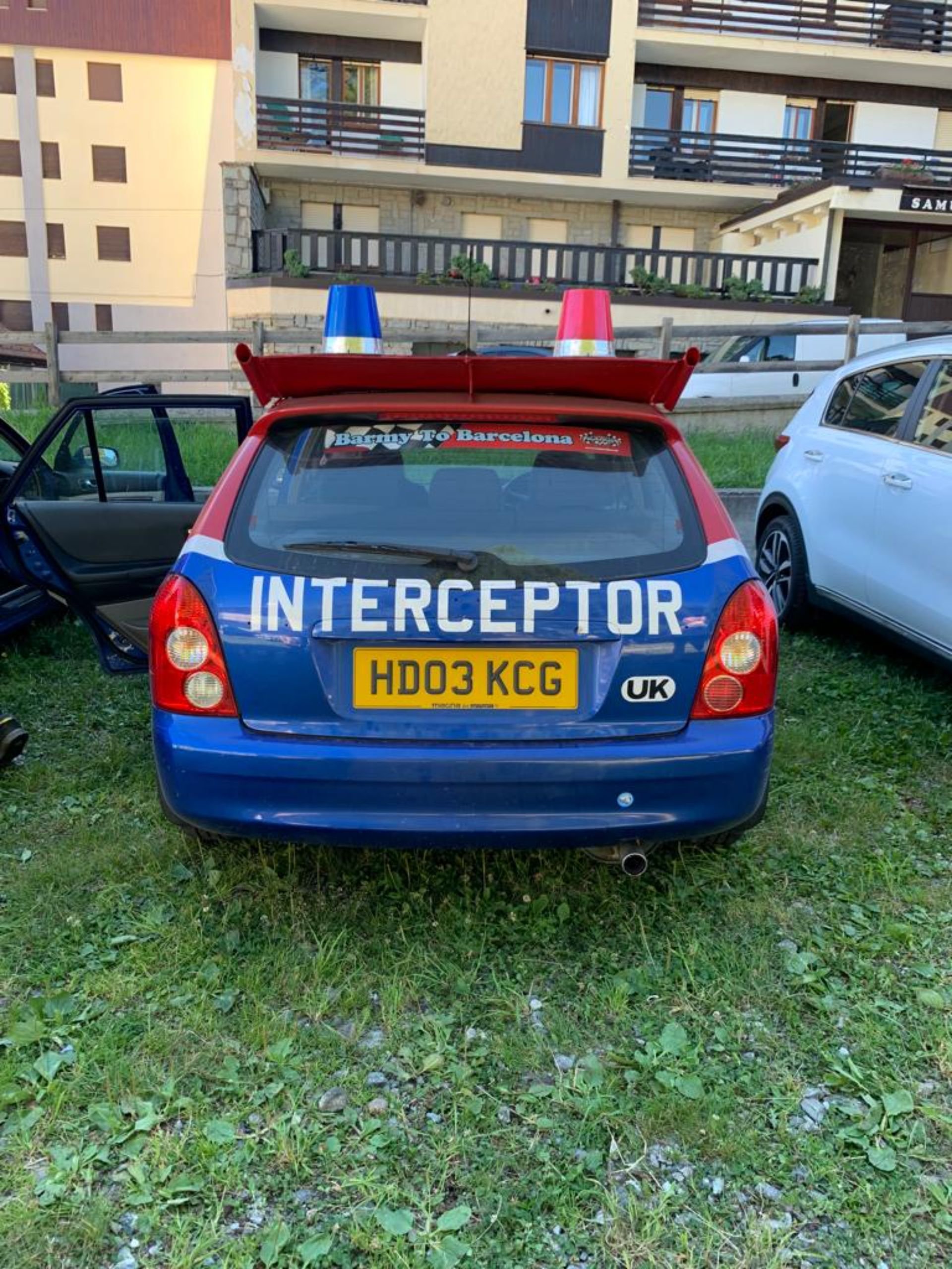 A blue emergency responder vehicle with a yellow license plate, parked on grass, with the word 'INTERCEPTOR' displayed on the back and large red and blue lights on the roof.