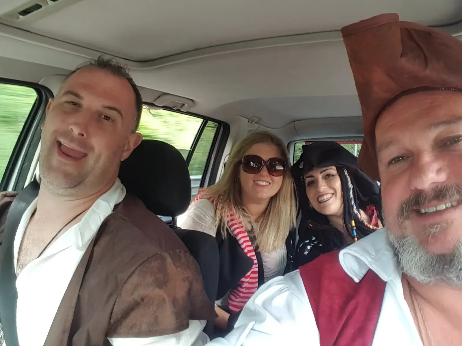 Four people dressed as pirates taking a selfie inside a vehicle.