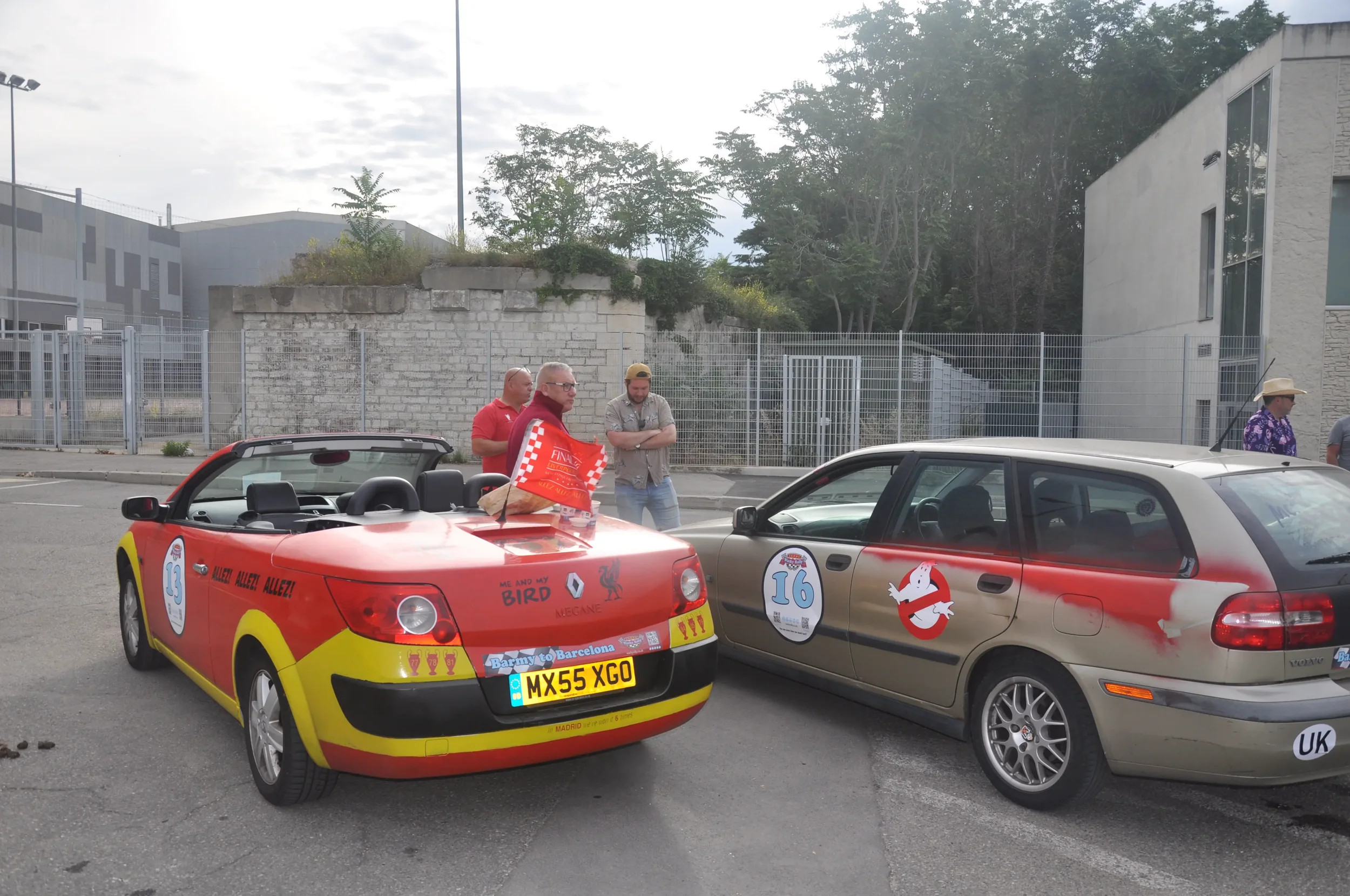 Two cars decorated with themed decals from popular movies or cartoons, parked outdoors near a fenced area, with four men standing nearby, one wearing a cowboy hat and a purple shirt, during daytime.