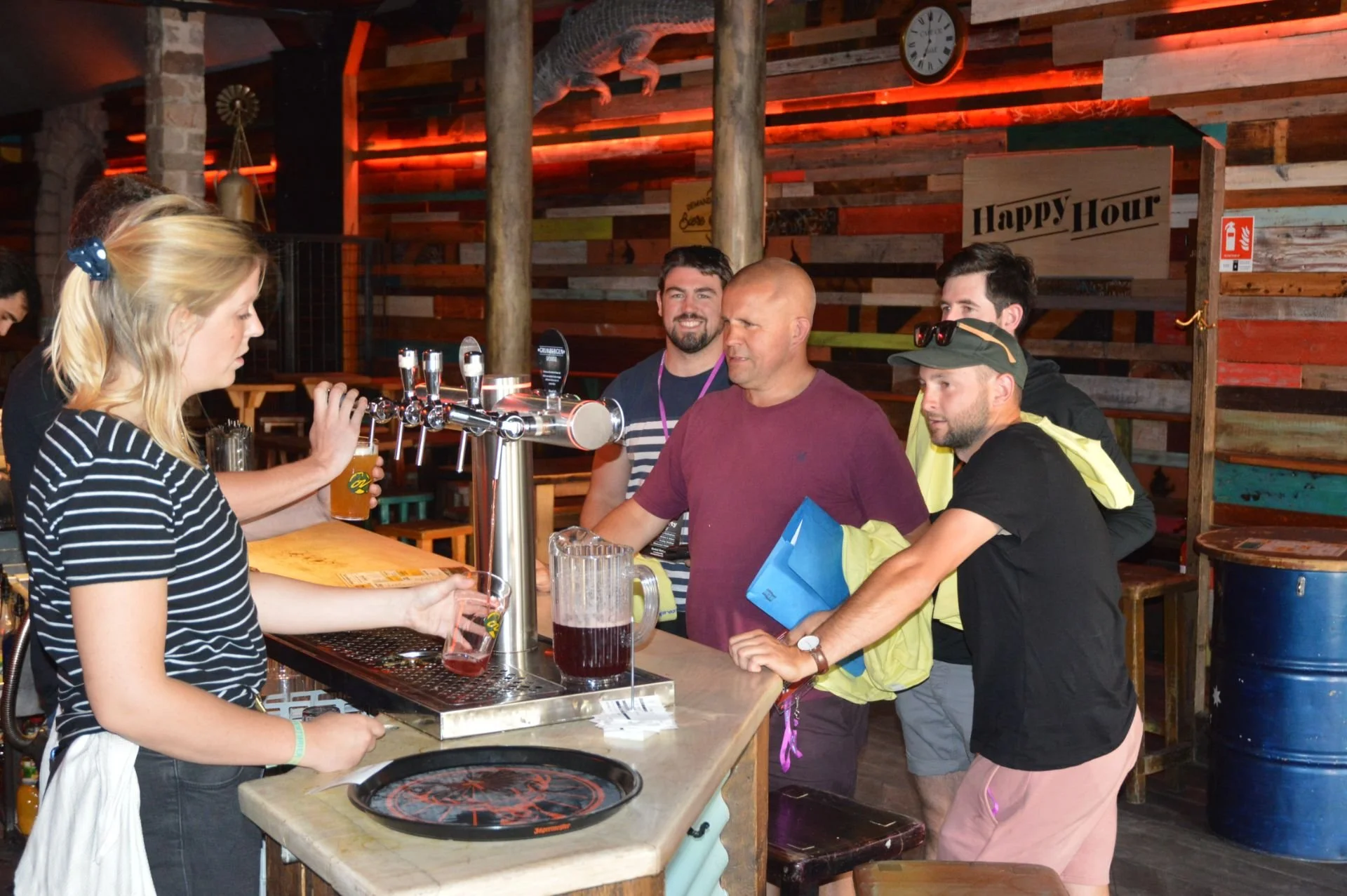 A woman serving beer at a bar with three men waiting to order. The bar has a rustic wood decor with a 