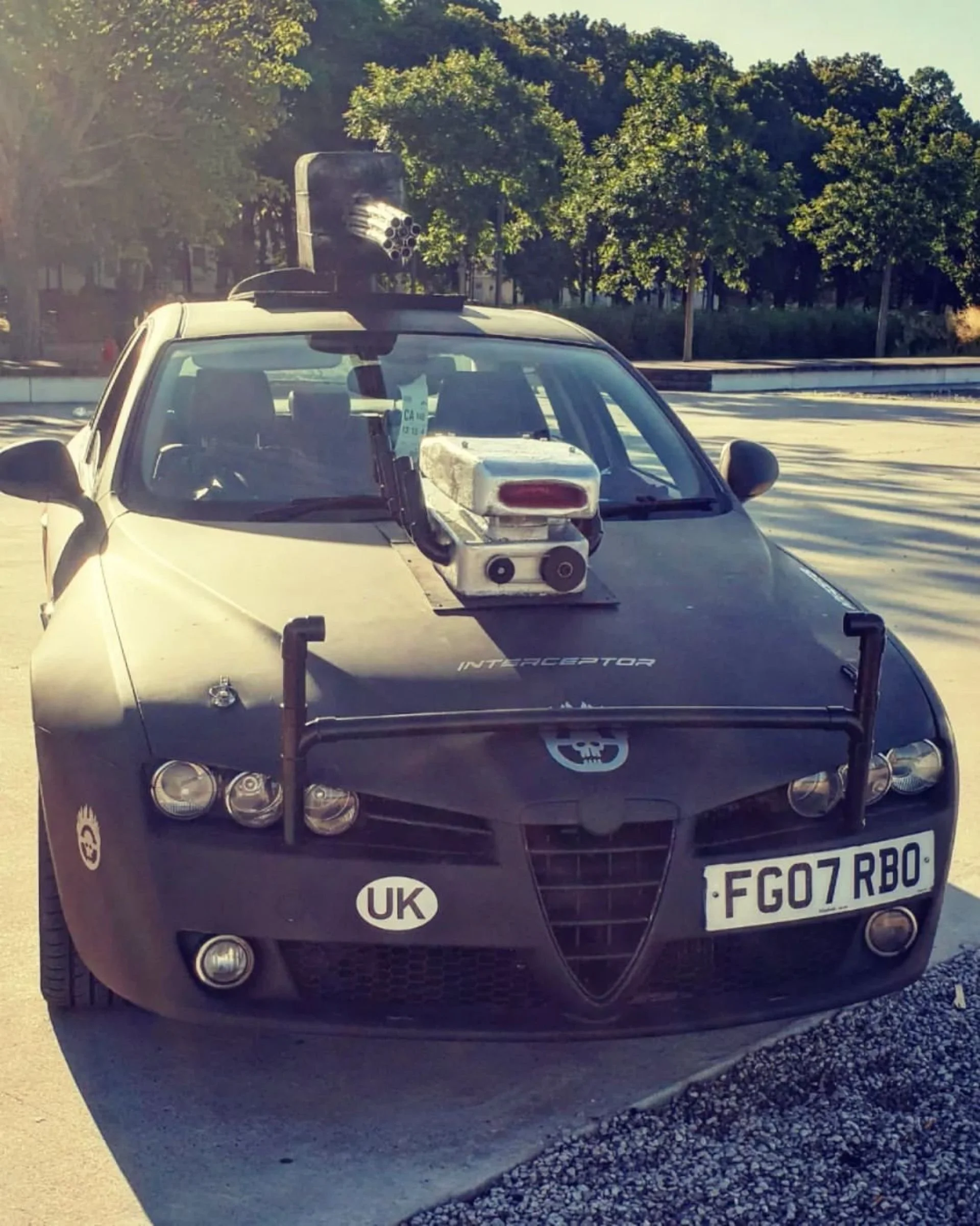 A black car with police-style equipment and various devices mounted on the hood and roof, resembling a homemade or modified police vehicle.