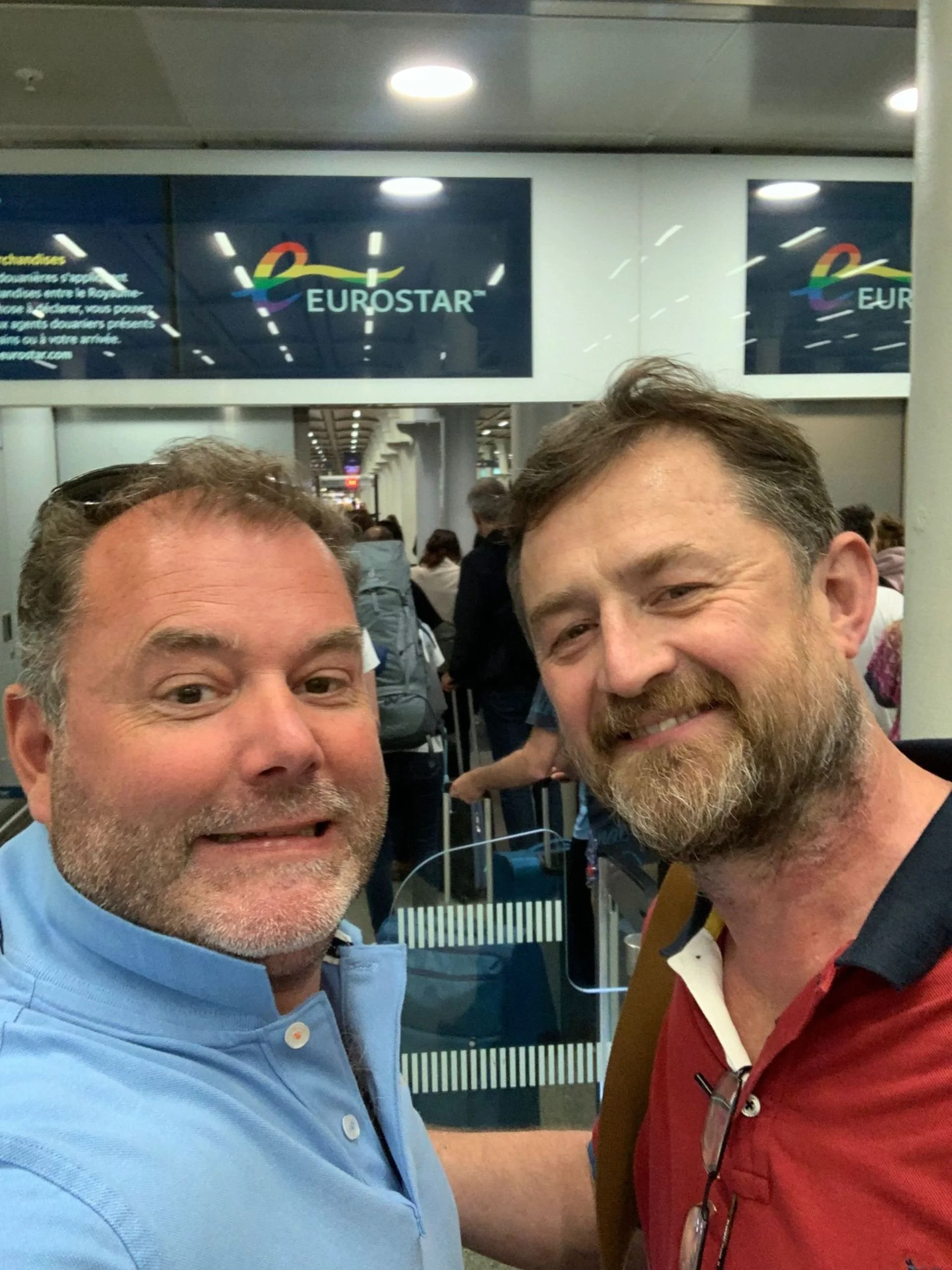 Two men smiling at the airport, with a Eurostar sign visible in the background.