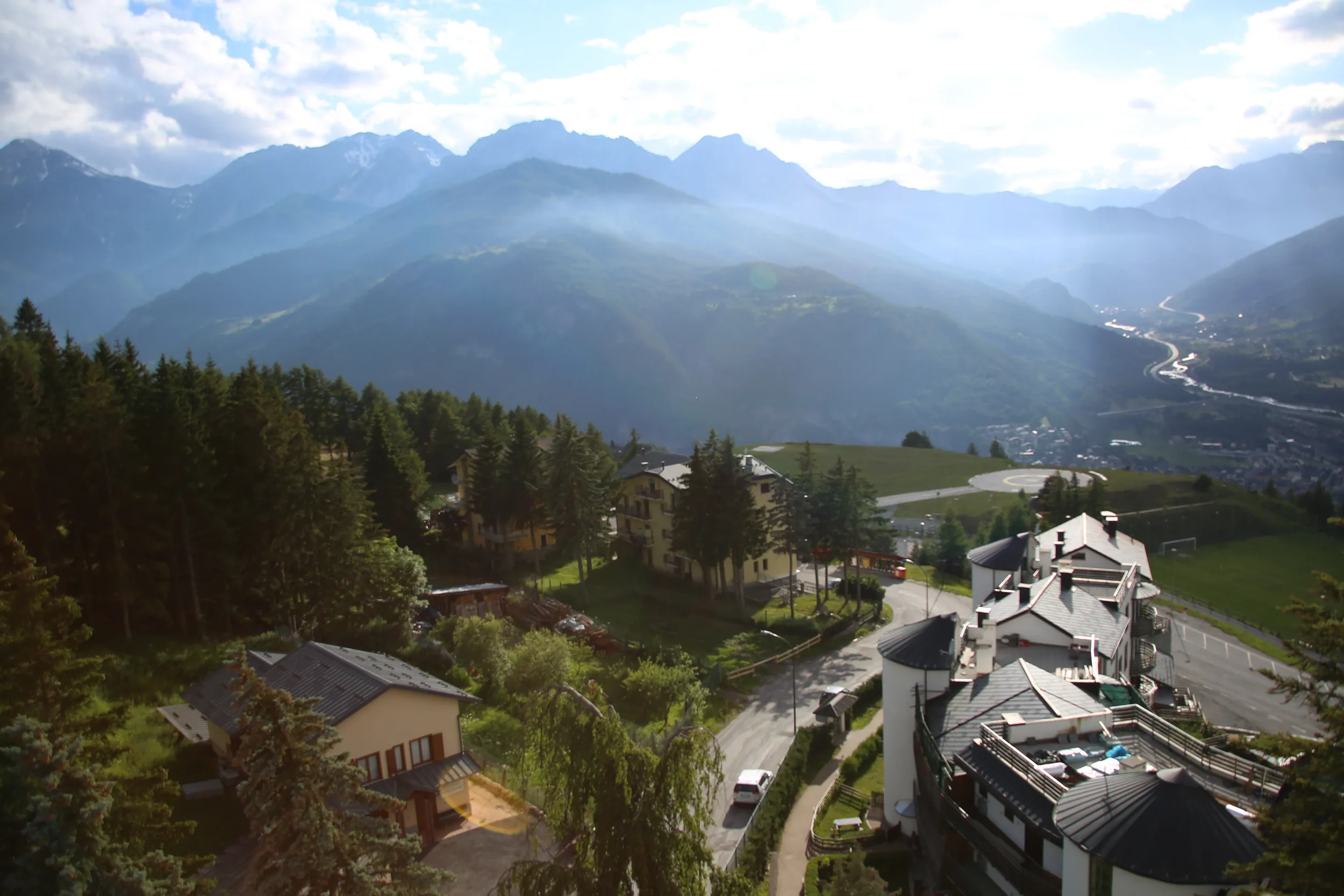 Scenic view of a mountain landscape with houses, roads, a river, and a forested hillside.