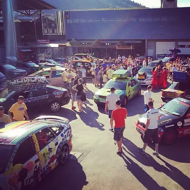 A busy parking lot filled with various cars and numerous people walking around on a sunny day at a commercial area.