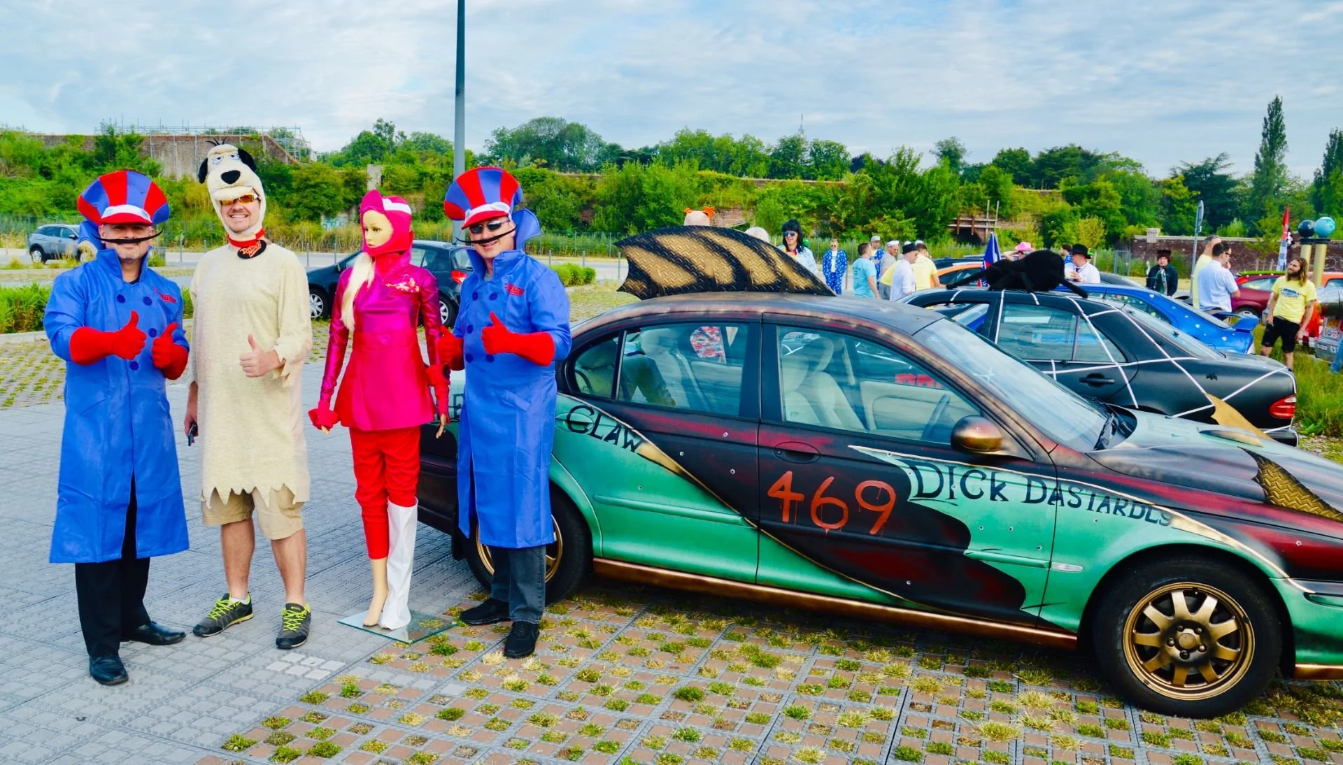People in costumes standing beside decorated car at an outdoor event.