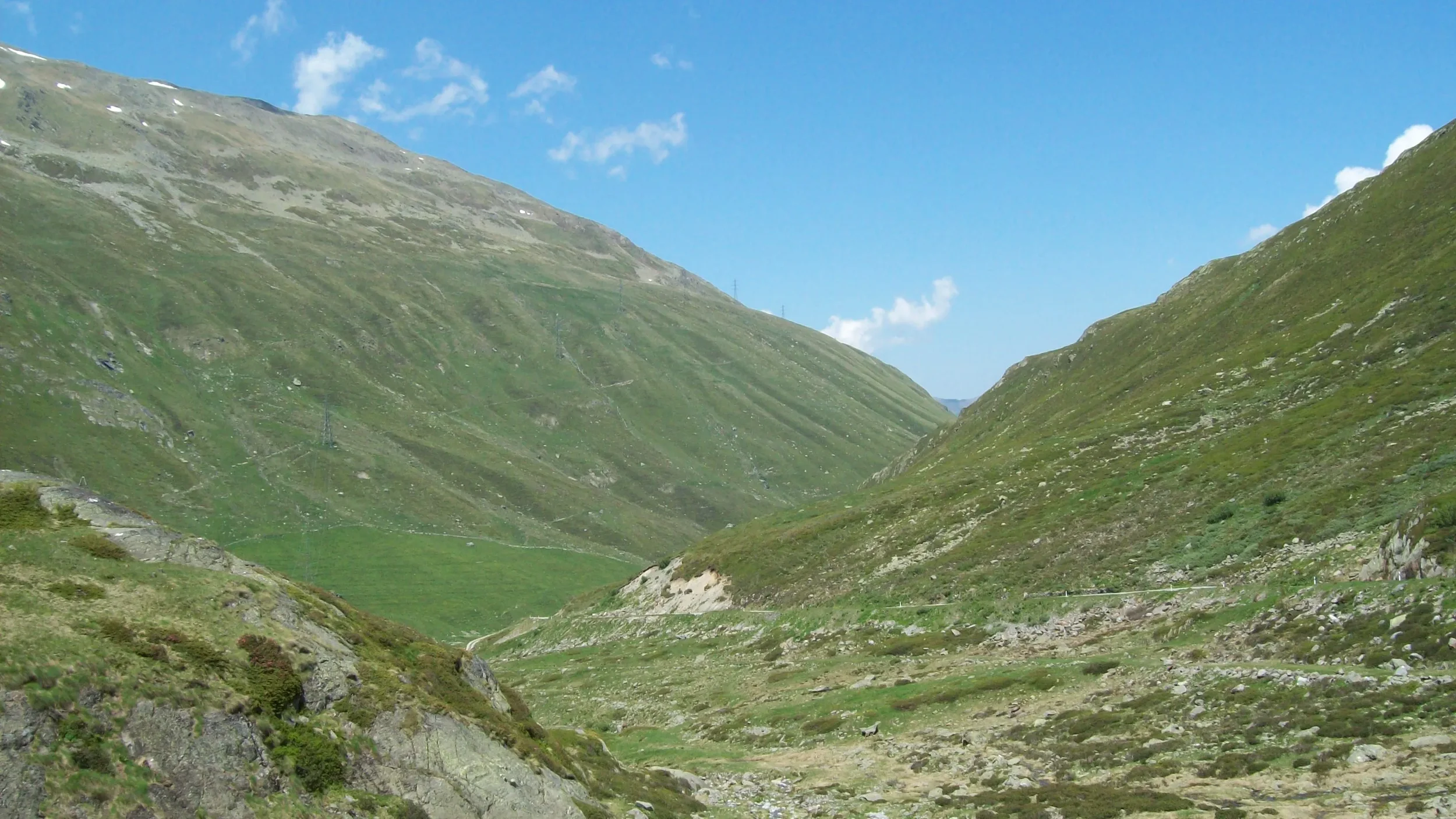 A mountain valley with green grassy slopes and a clear blue sky.