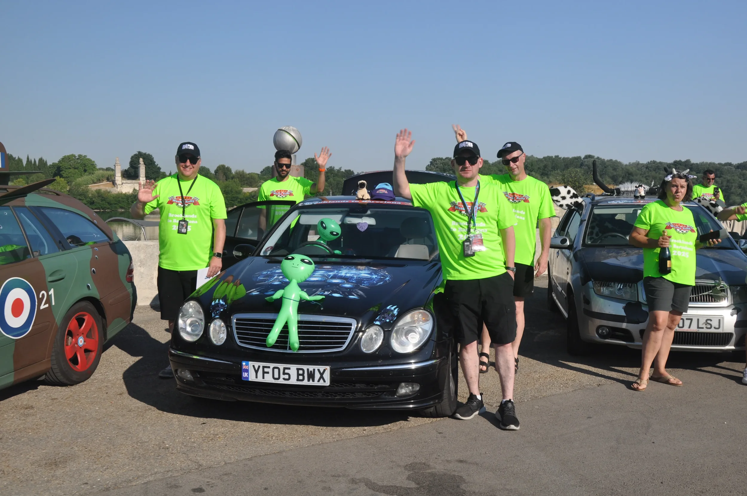 Group of people in bright green T-shirts standing beside decorated cars at an outdoor event.