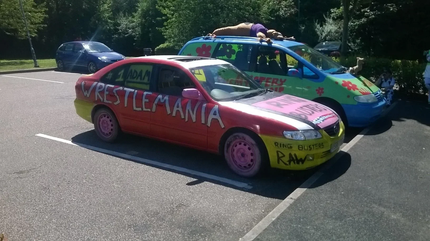 Colorful decorated cars in a parking lot with trees in the background, including a red car with 